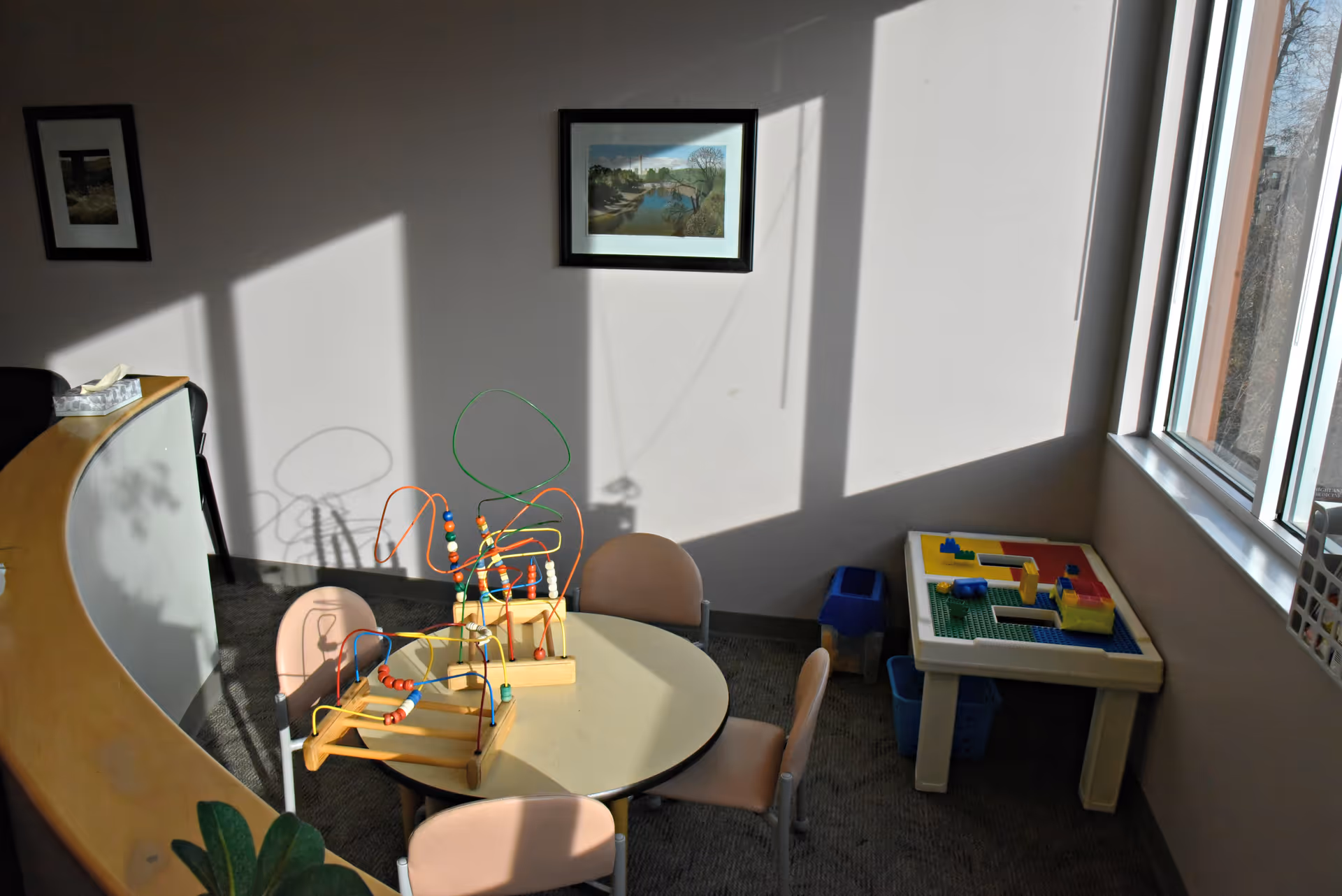 Sunlit interior activity room with a round table, bead maze toys, and kid-sized chairs.