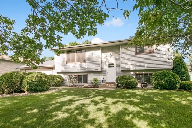 Two-story light-gray residential building with a well-kept lawn and trimmed shrubs in front.