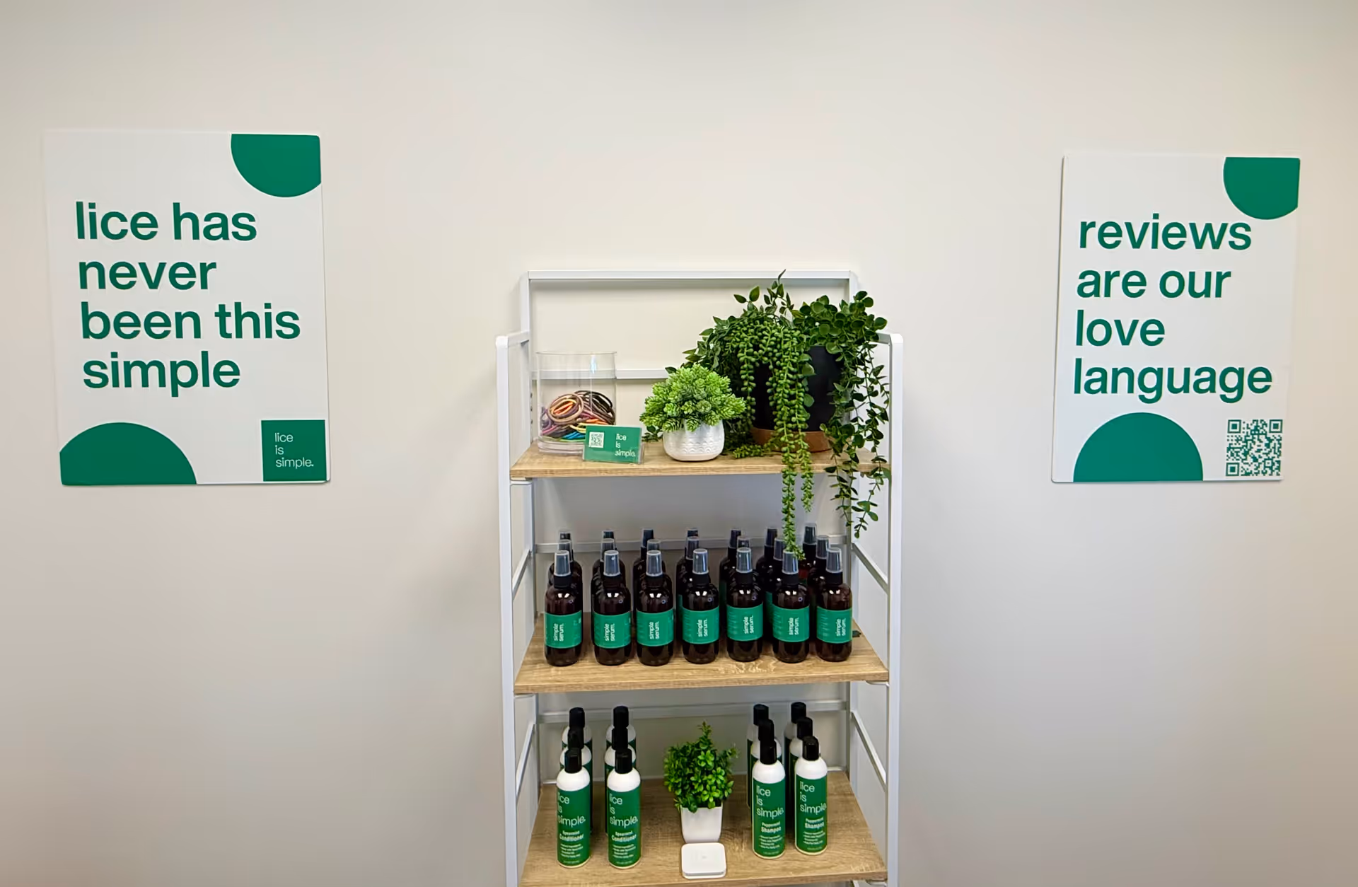 Interior wall with a metal shelf of bottles, plants, and green 'Lice is Simple' signs.