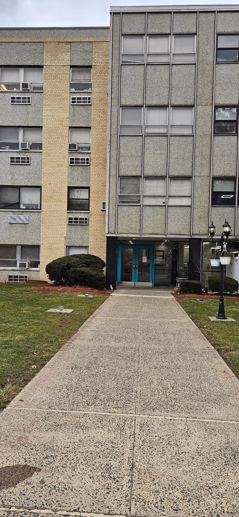 Front entrance of Windsor Gardens Care Center with a concrete walkway and tall windows.