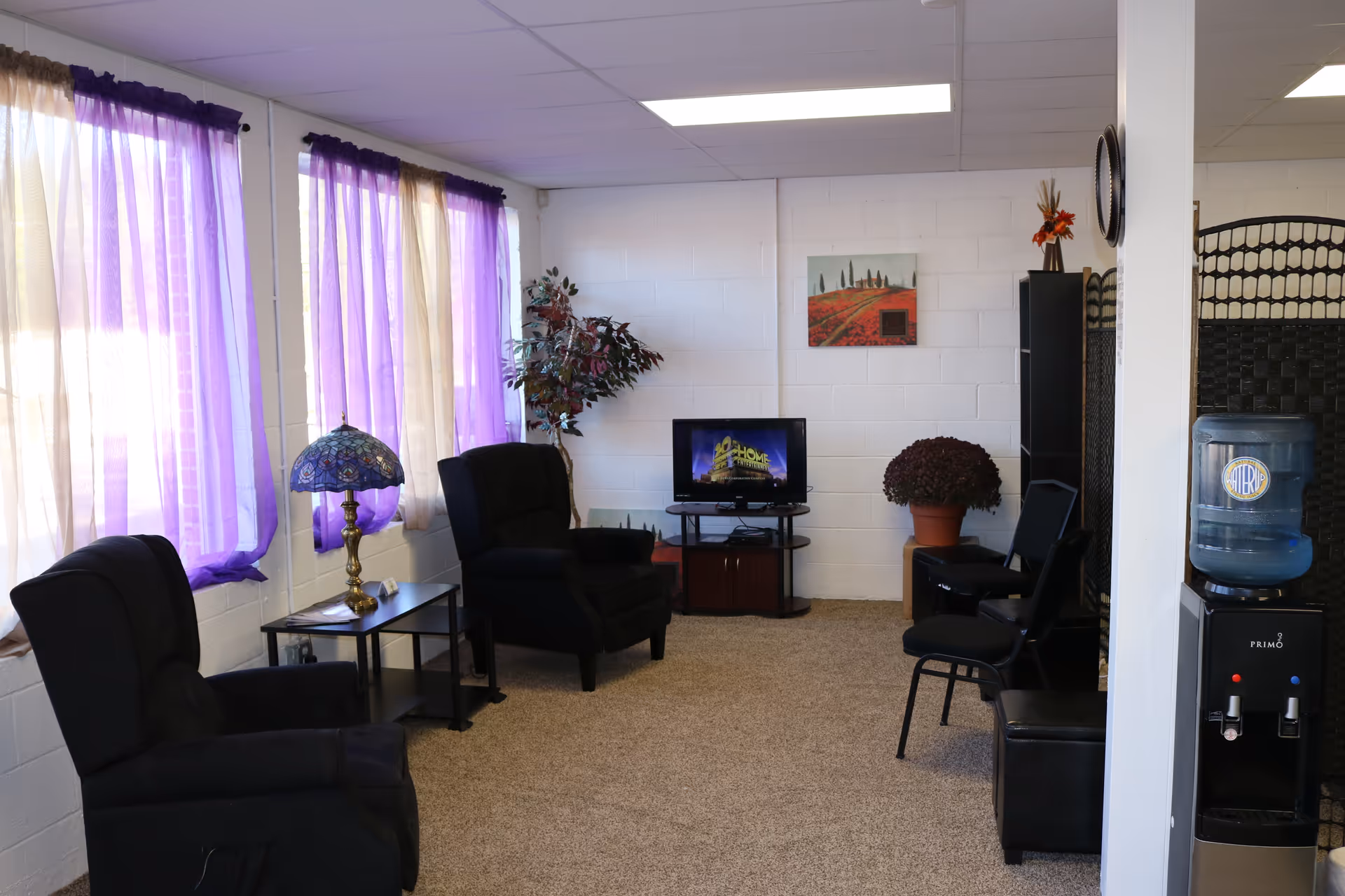 A cozy lounge in a senior facility with purple curtains, black chairs, and a small TV.