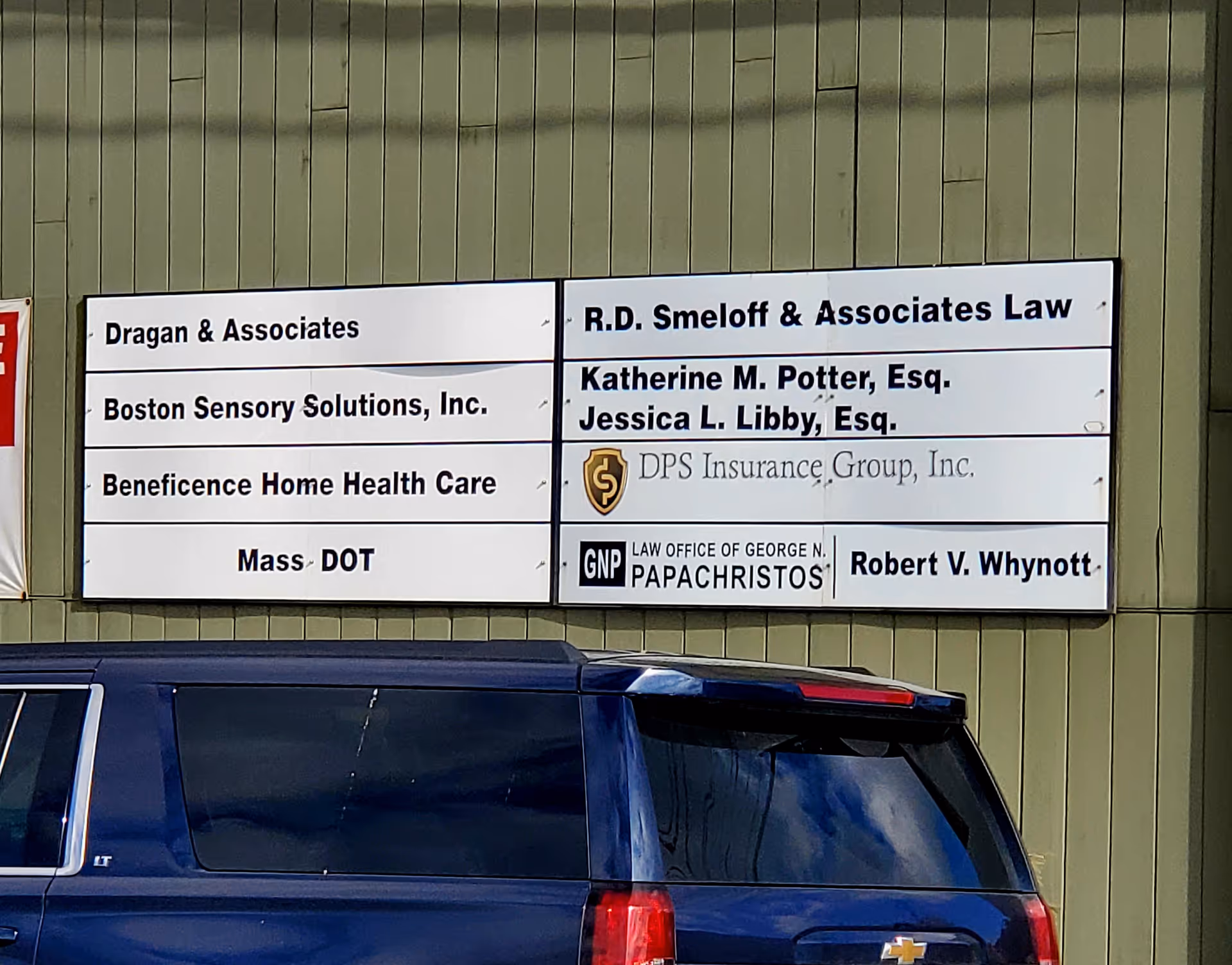 Exterior wall with signboards including Beneficence Home Health Care and a blue SUV