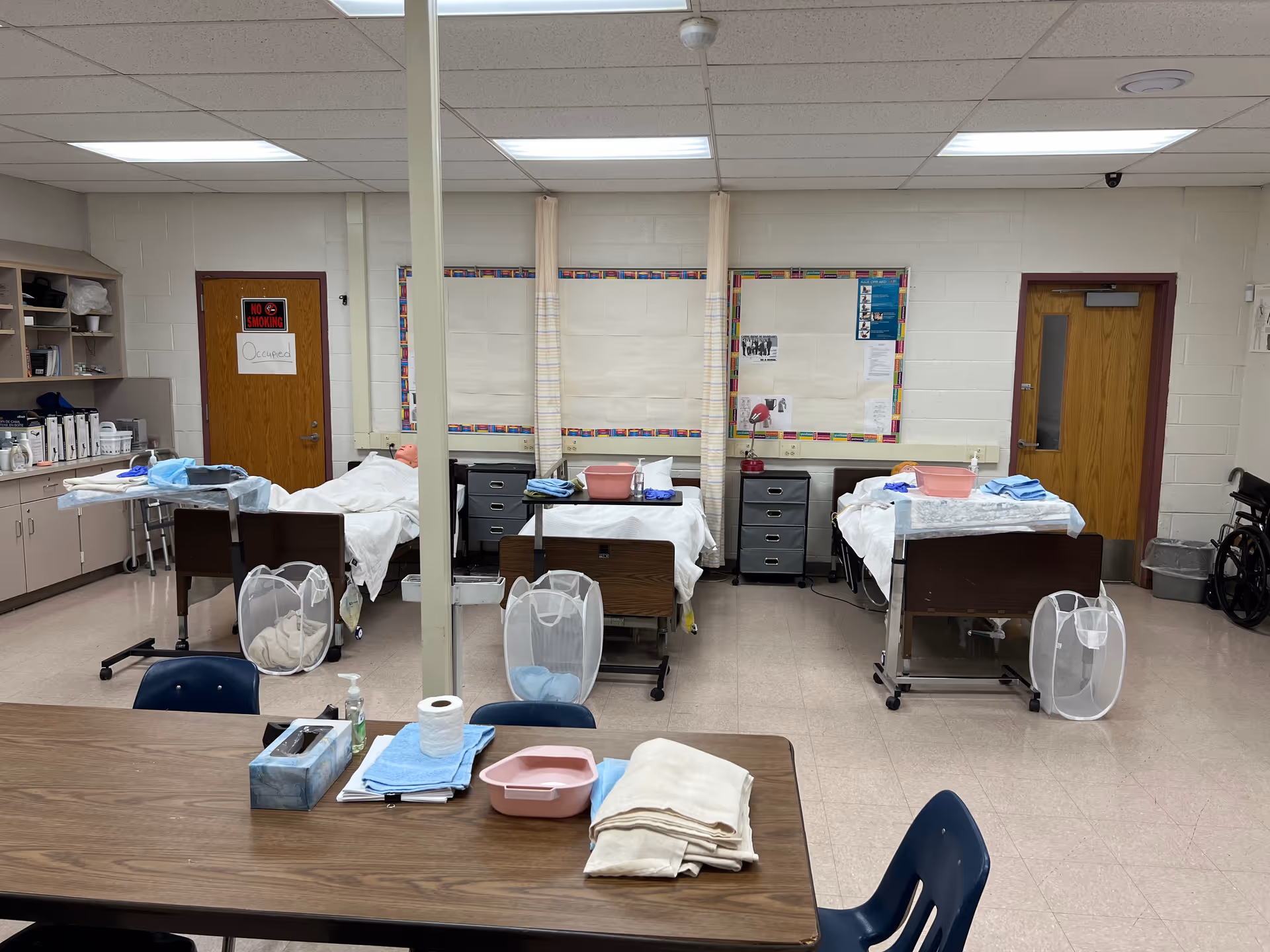 Clinical training room with multiple patient beds and nursing supplies along the back wall.