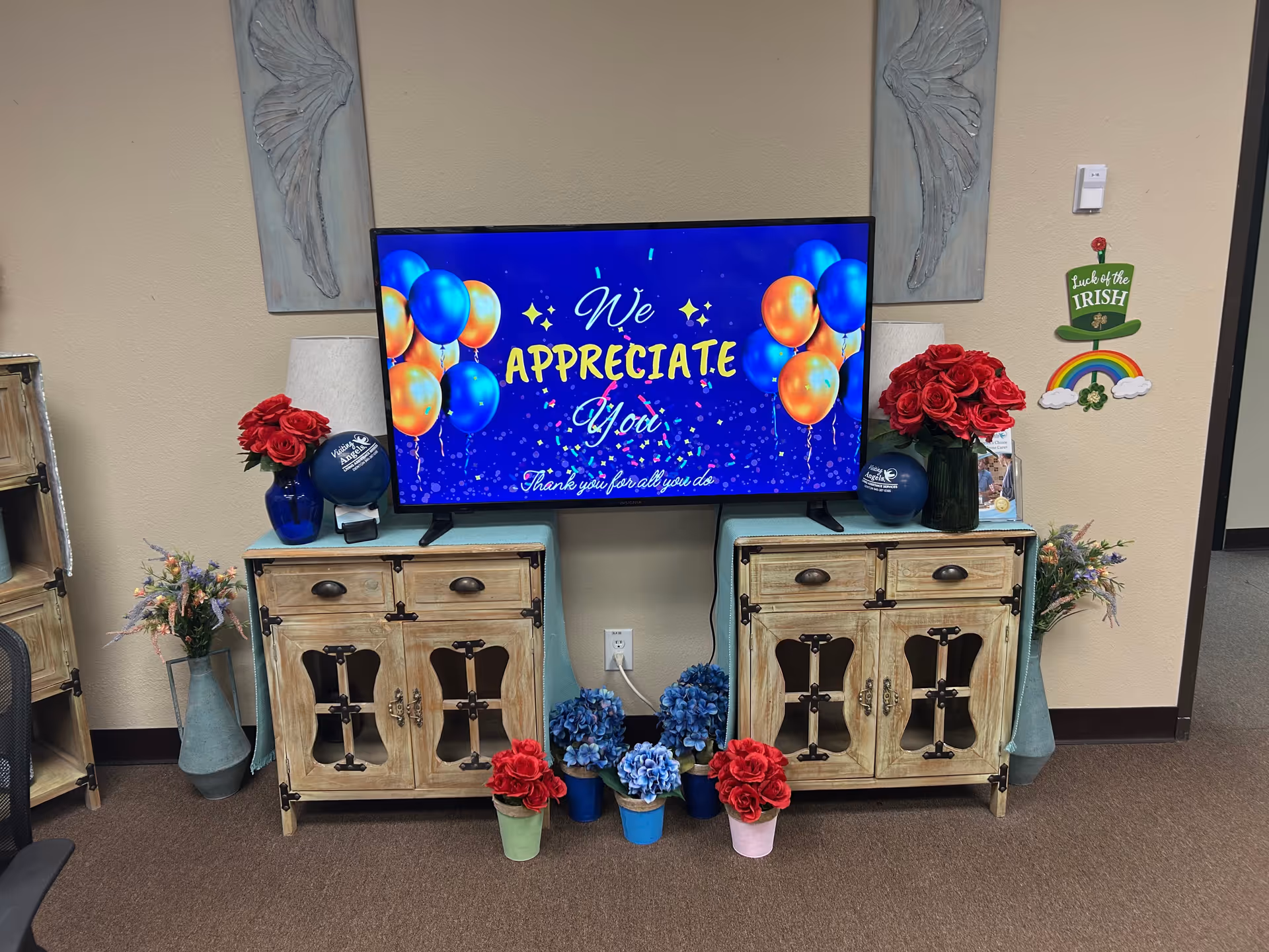 TV screen displays 'We appreciate you' with balloons and flowers on rustic cabinets.