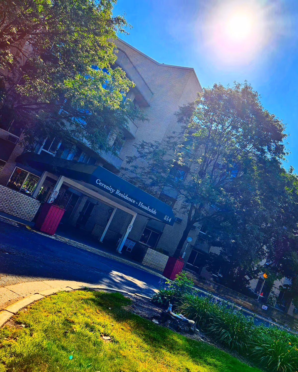 Exterior view of Cerenity Residence on Humboldt, showing the entrance under a blue awning and trees.