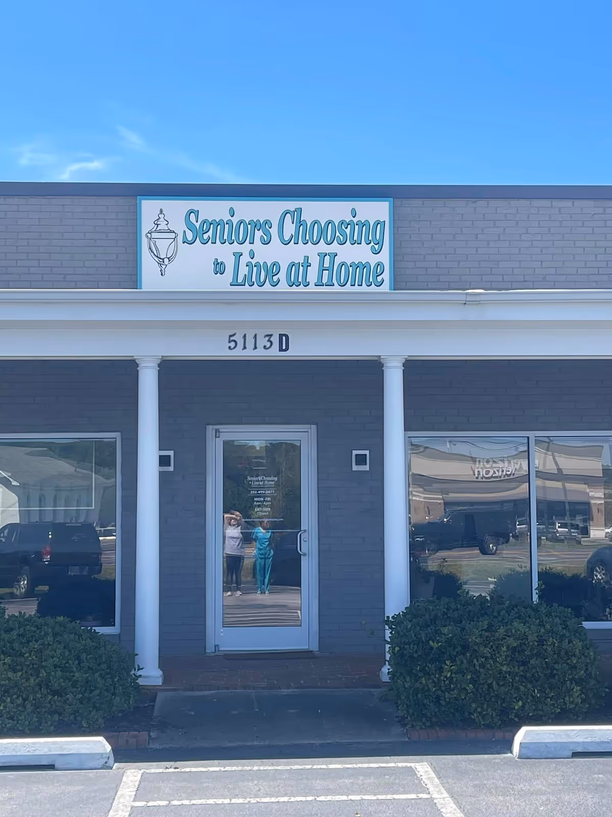Front of a facility with a sign reading 'Seniors Choosing to Live at Home' and entrance.