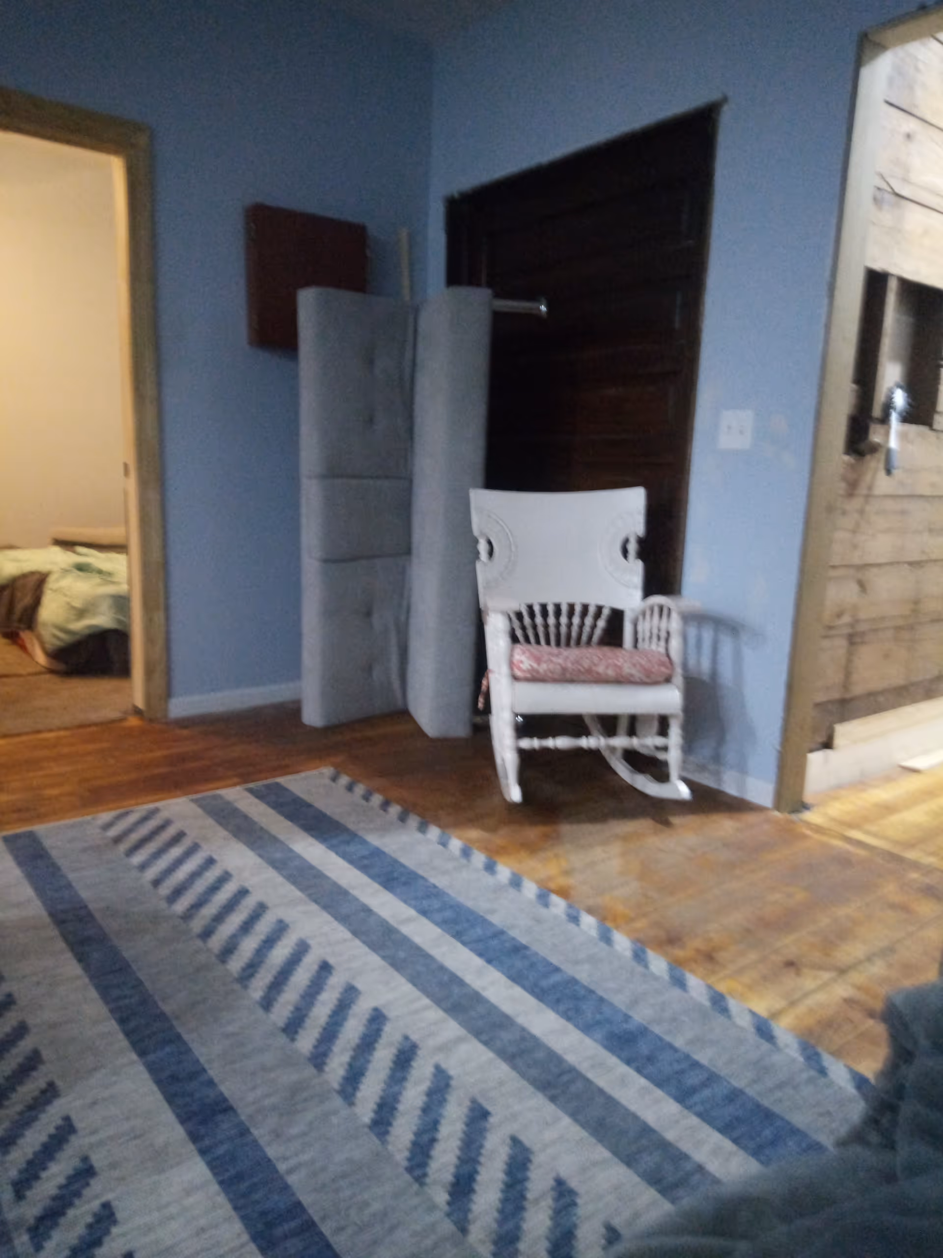 Blue-walled interior with a rocking chair, stacked cushions, and striped rug.