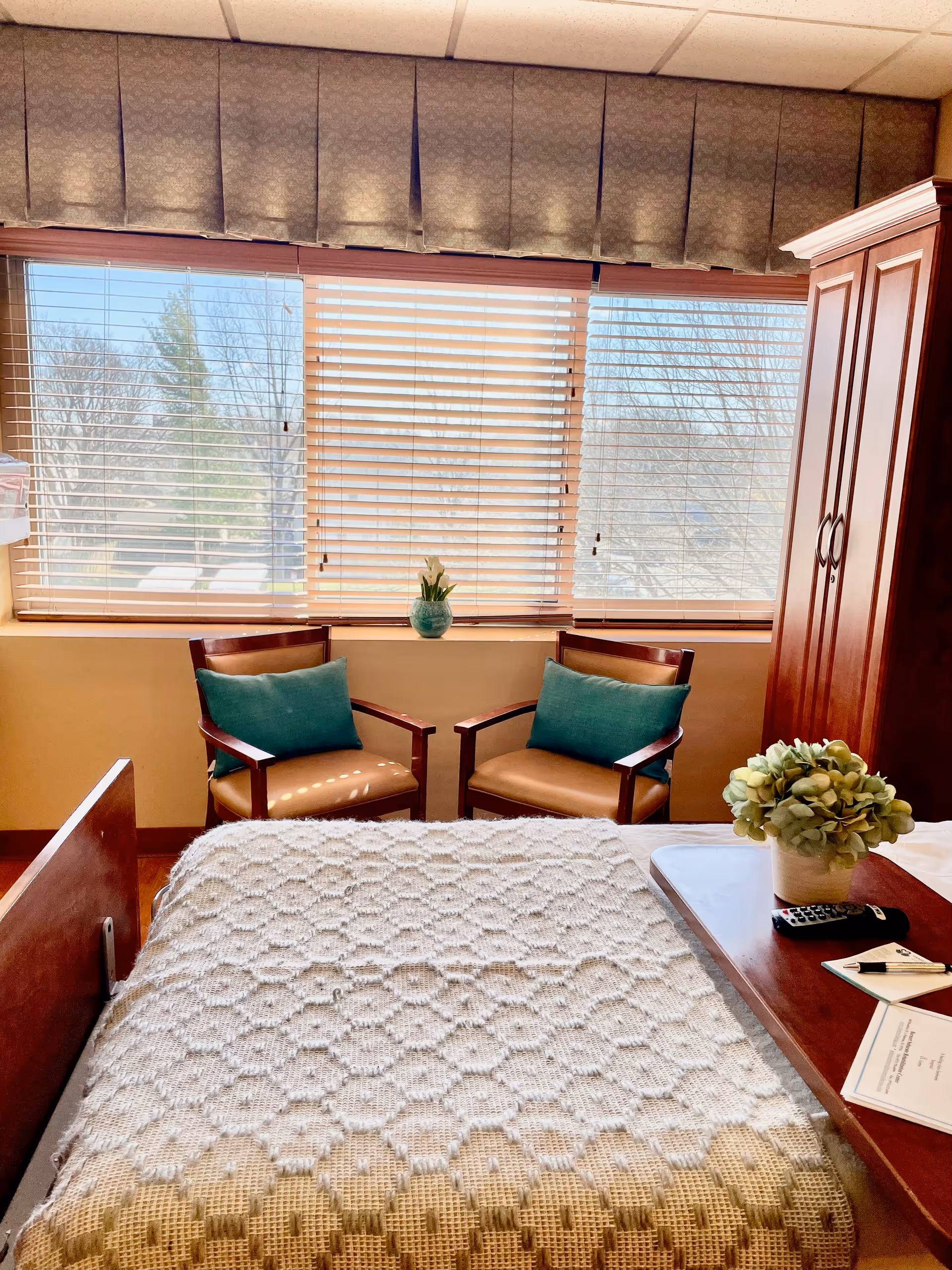 A senior living facility bedroom with a bed, two chairs, and a window.