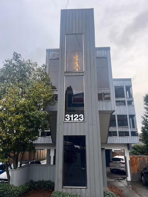 Tall gray modern building facade with large glass windows and the number 3123.