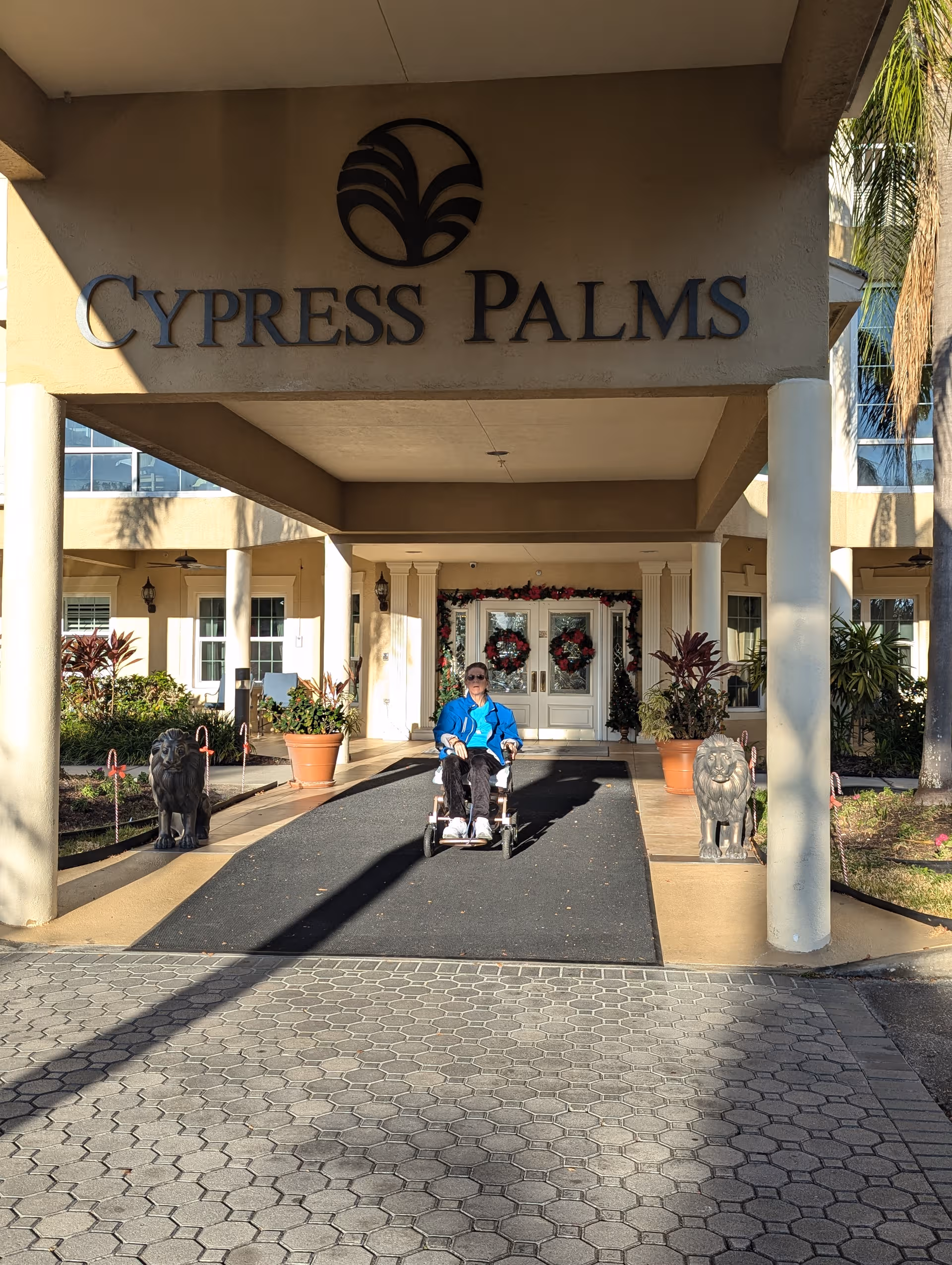Front entrance of Cypress Palms with a resident in a wheelchair under the porte-cochère.