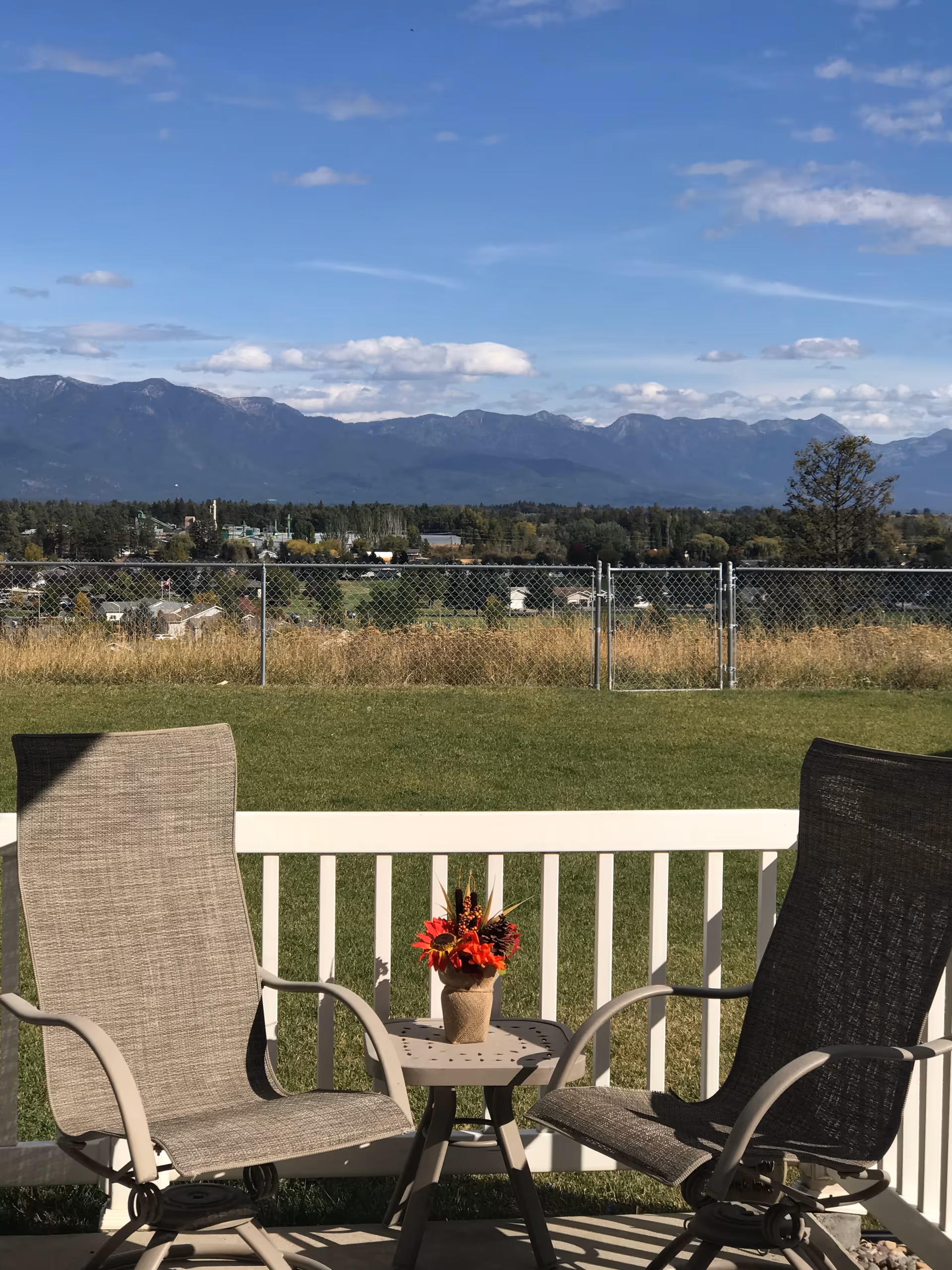 Outdoor patio with two chairs and a small table with a flower planter, mountains in distance