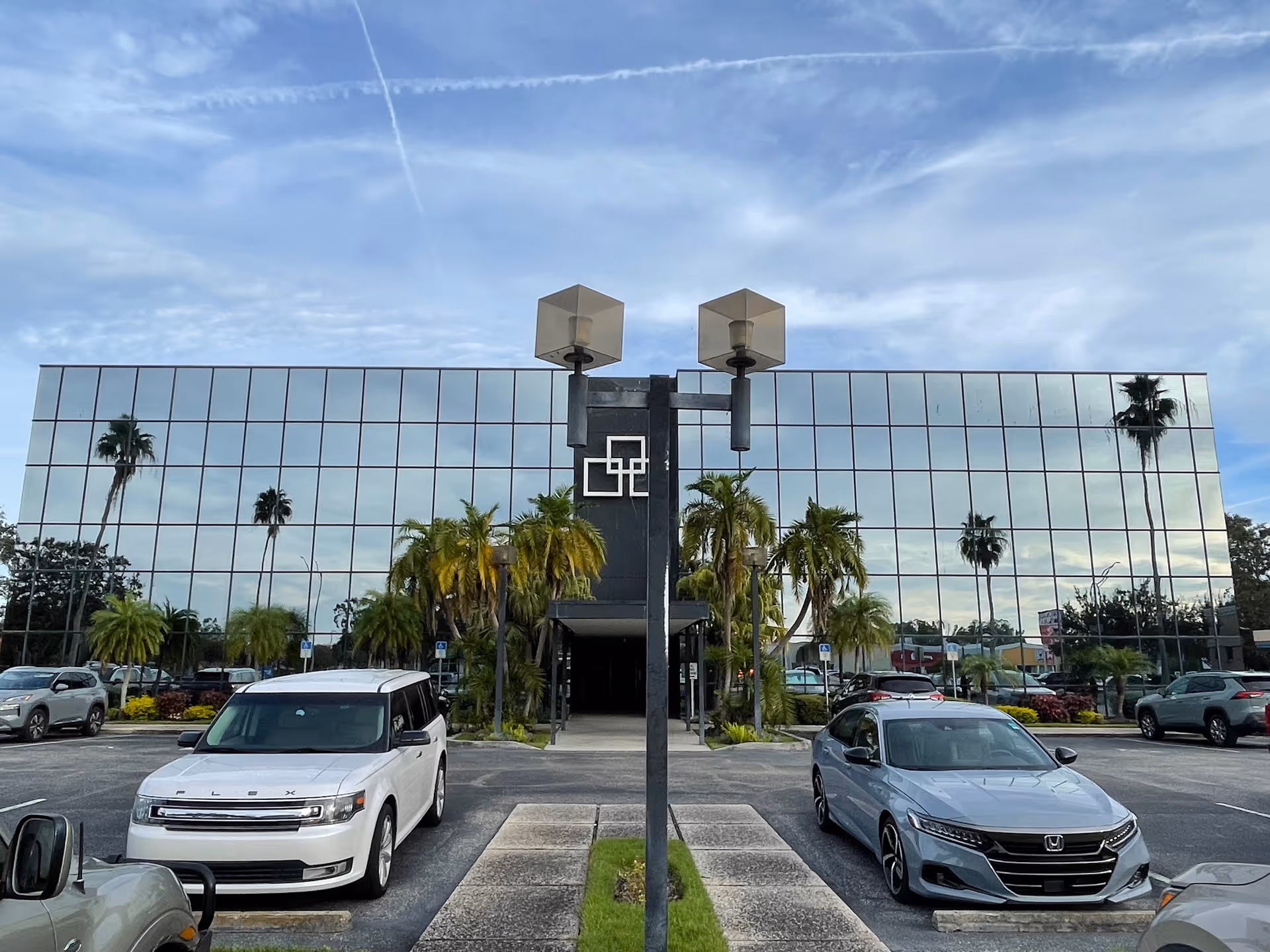 Front of a glass-paneled building with palm trees and a parking lot.
