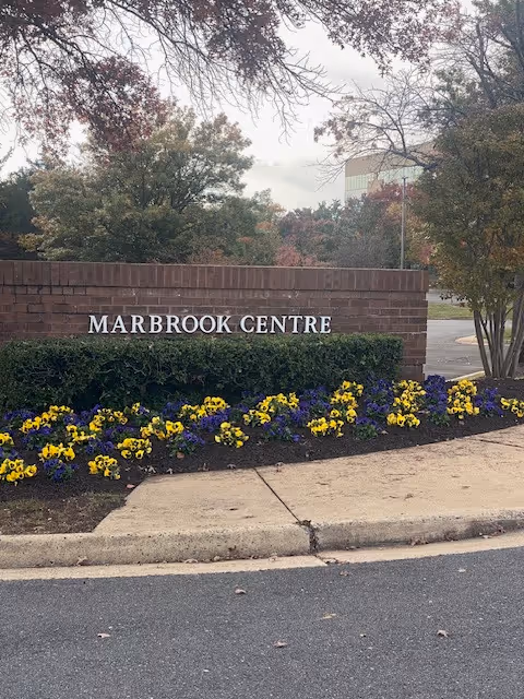 Brick sign reading MARBROOK CENTRE with flowers and a sidewalk in front