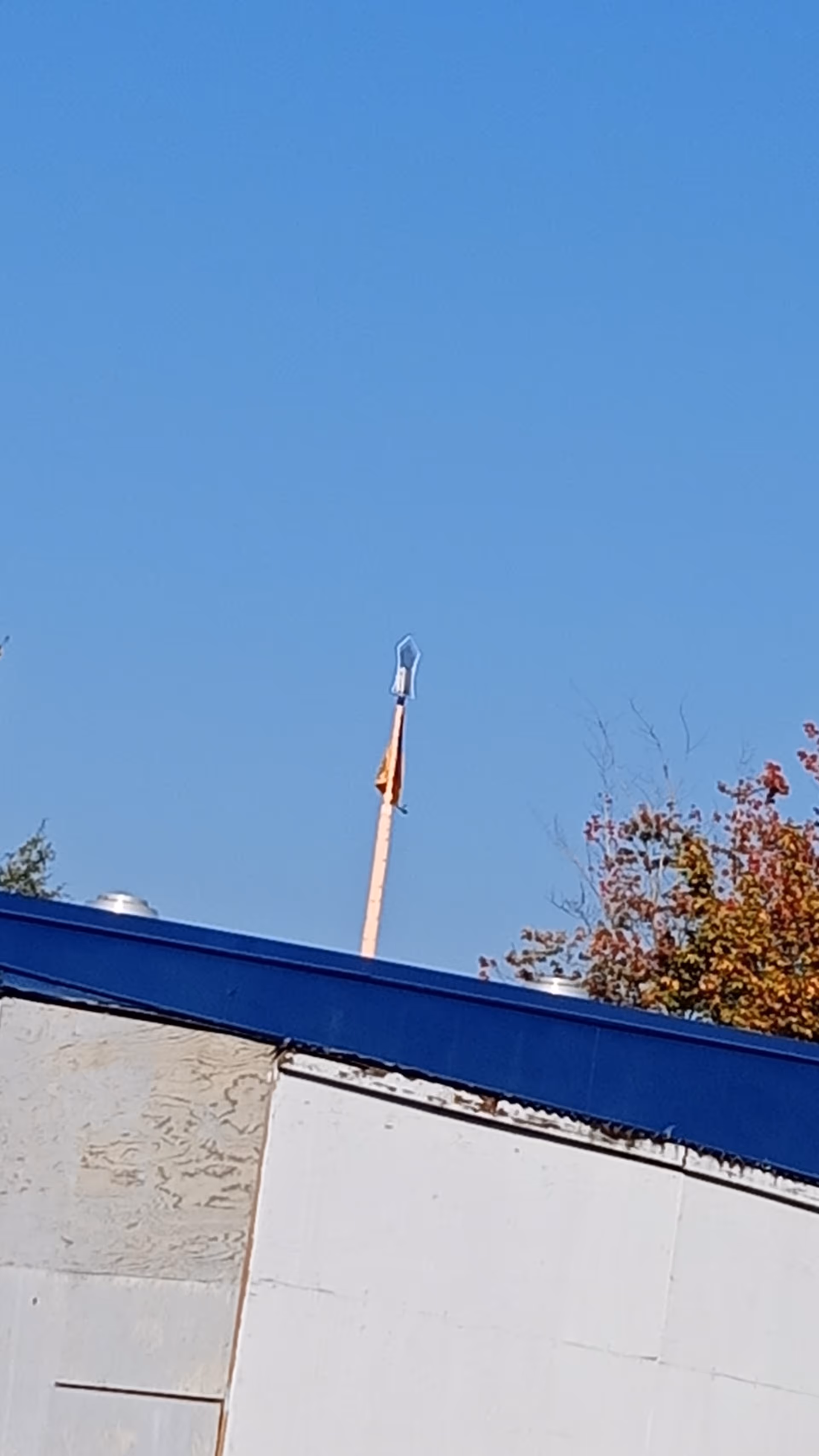 Clear blue sky over a building exterior with white panels and autumn trees.
