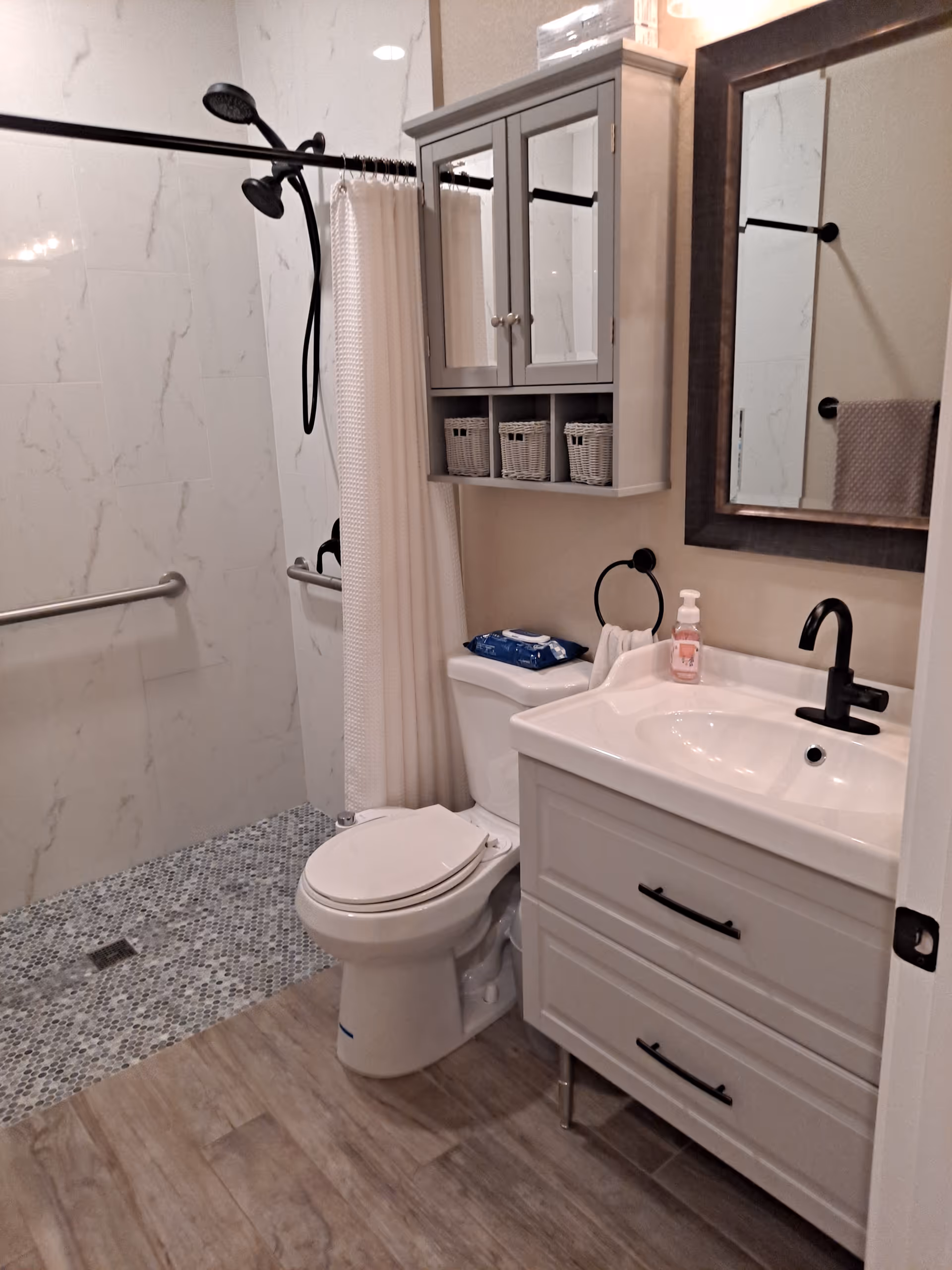 Accessible bathroom with shower, toilet, sink, and storage cabinet in a senior living facility.