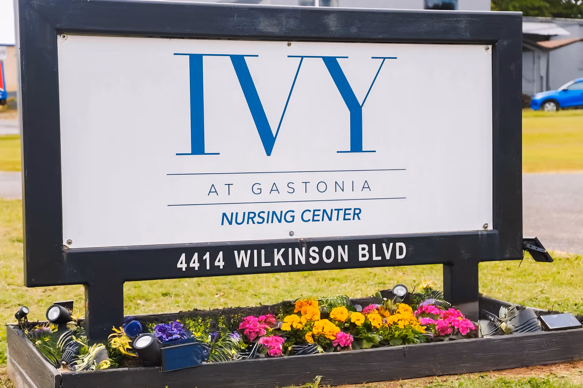 A roadside sign reading "IVY AT GASTONIA NURSING CENTER" with "4414 WILKINSON BLVD" and a flowerbed beneath it.