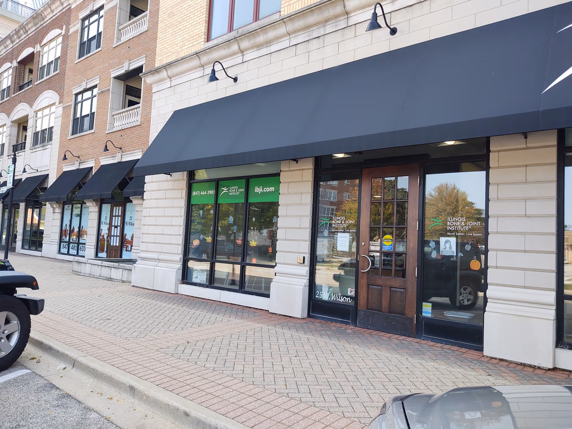 Exterior view of a row of storefronts with black awnings and glass doors.