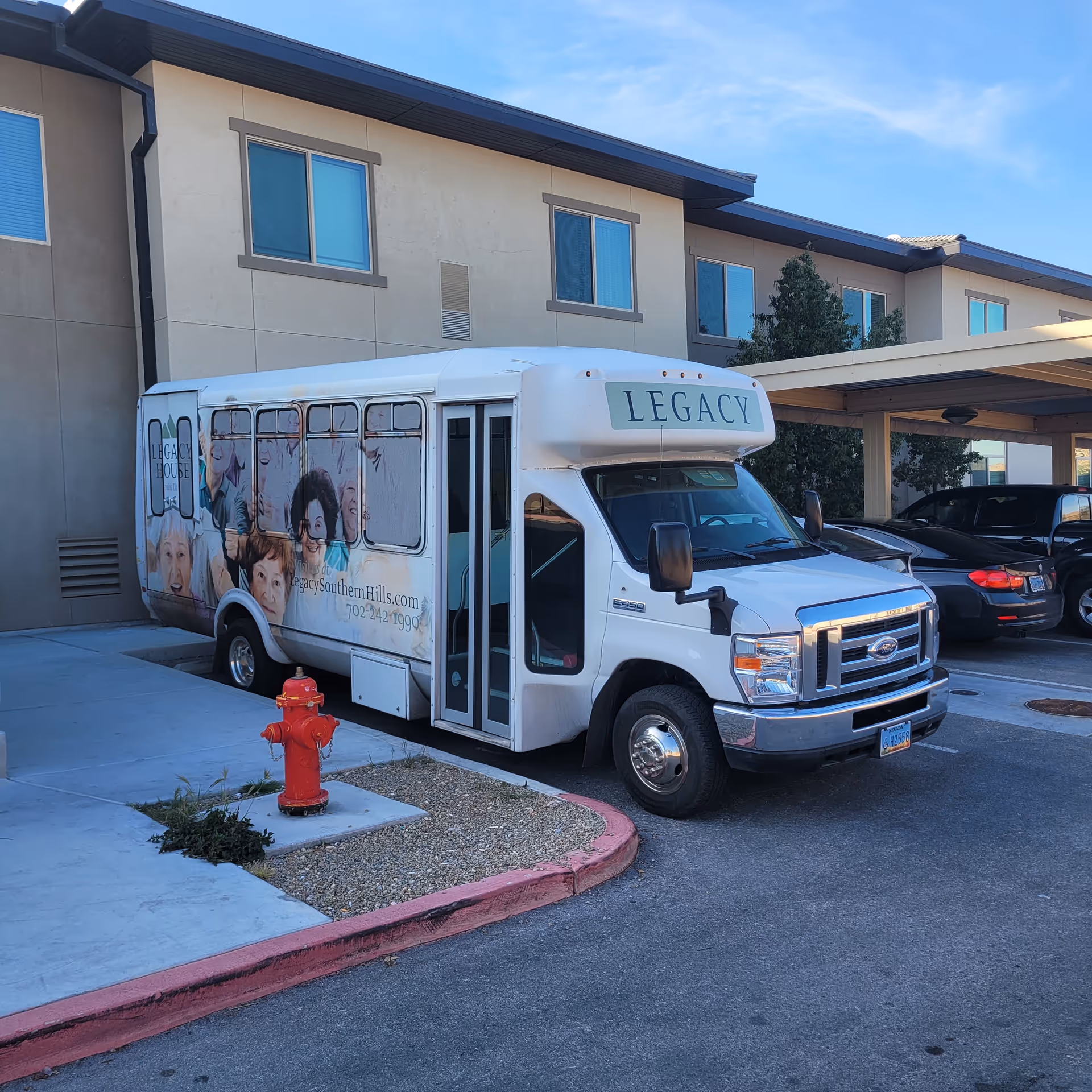 White Legacy bus with side photos parked outside a beige senior living building.