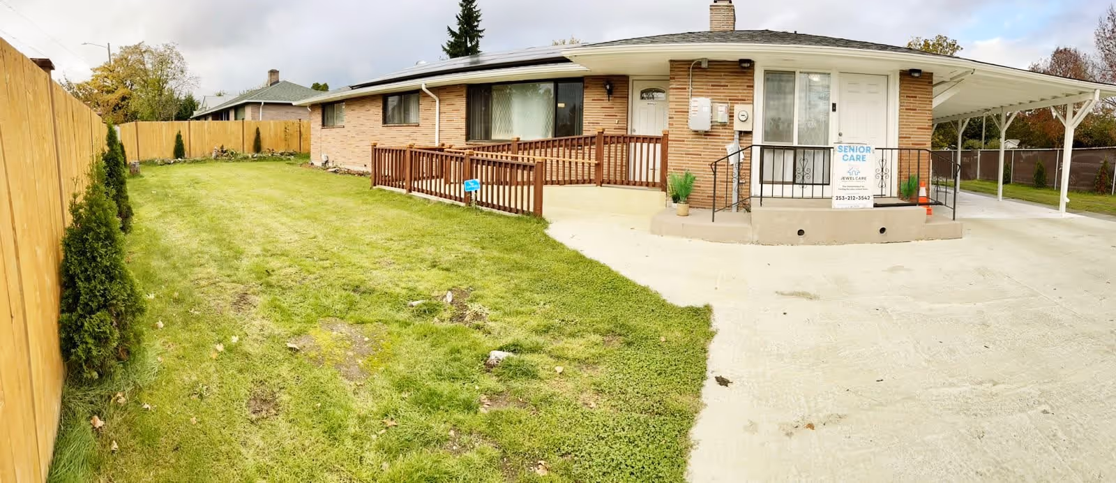 Front exterior of a single-story brick home with a green lawn, wooden accessibility ramp, carport, and a 'Senior Care' sign by the entrance.