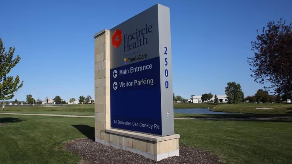 Tall Encircle Health sign on a sunny exterior with grass and a pond nearby.