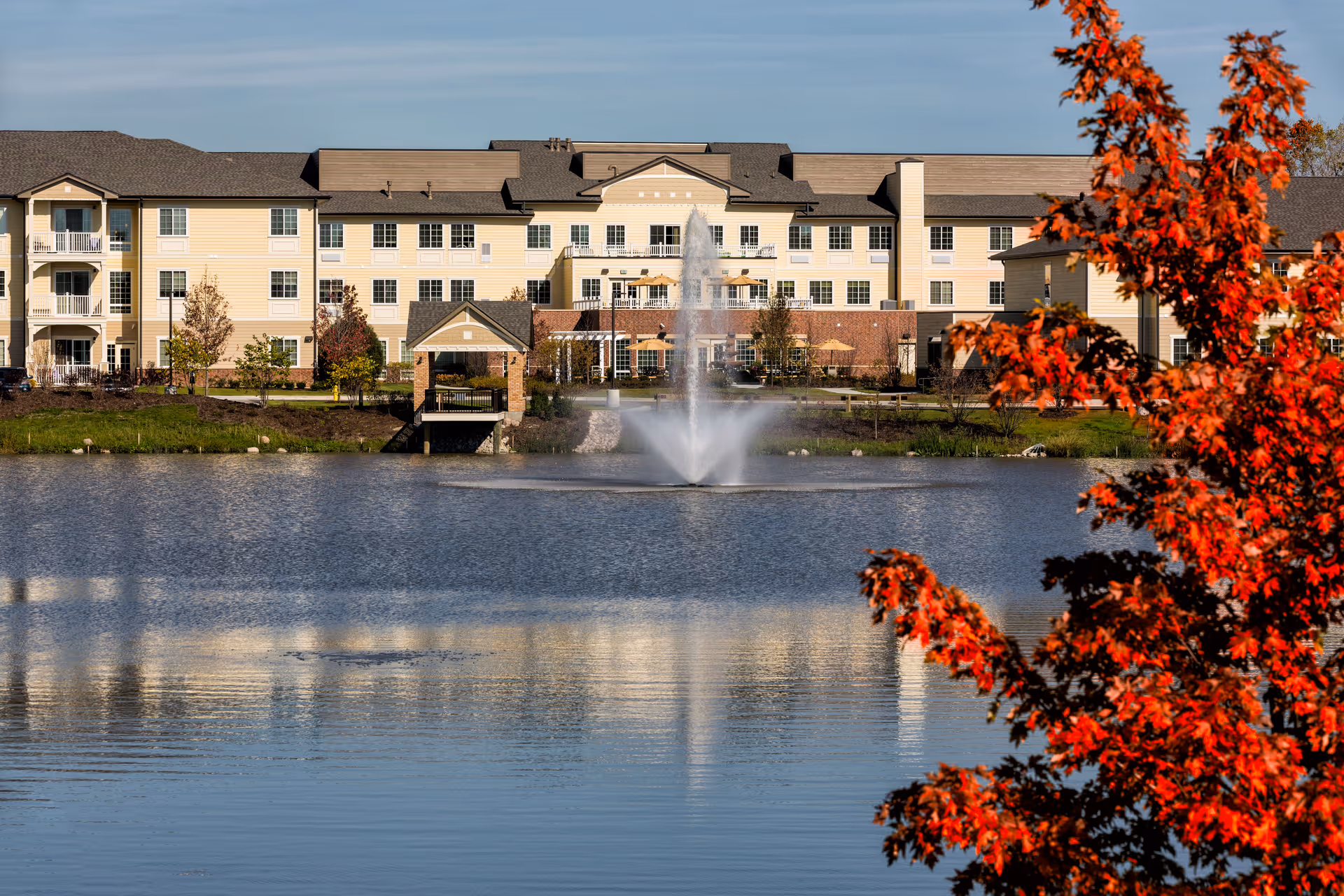 Exterior view of Green Oaks Senior Living across a lake with a fountain.