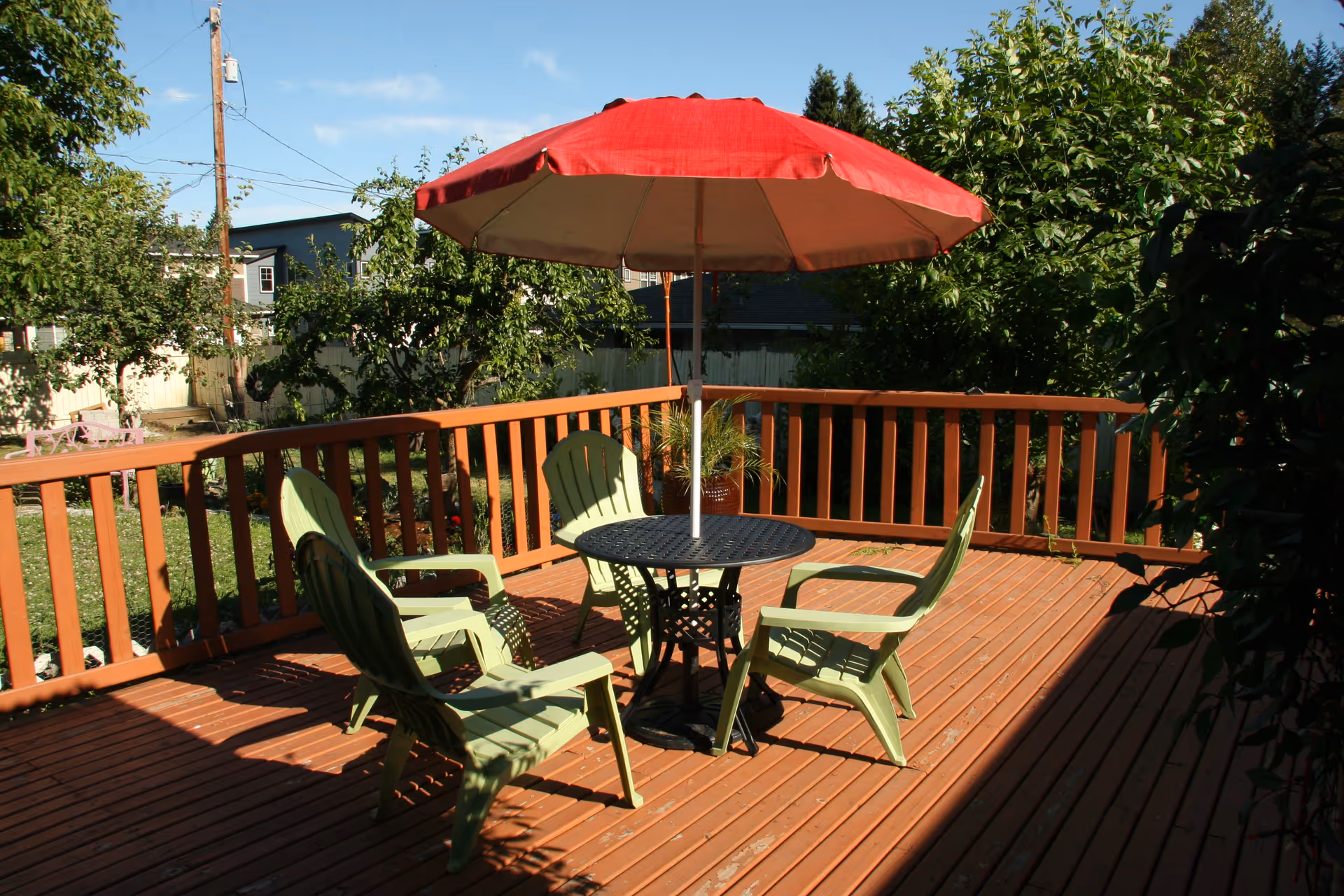 Outdoor wooden deck with a round table, four green chairs, and a red umbrella.