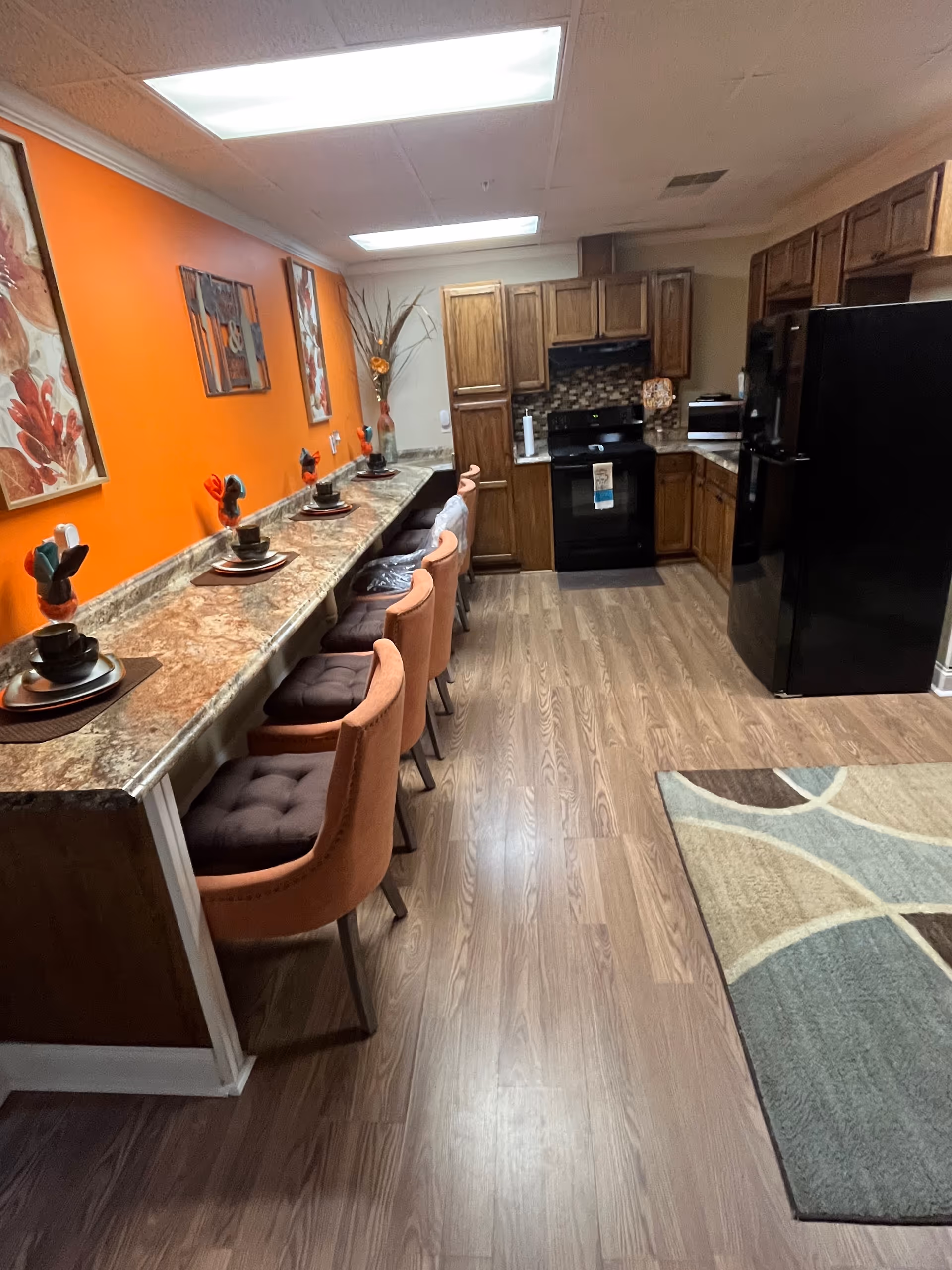 Long granite counter with stools along orange wall in a compact facility kitchen.