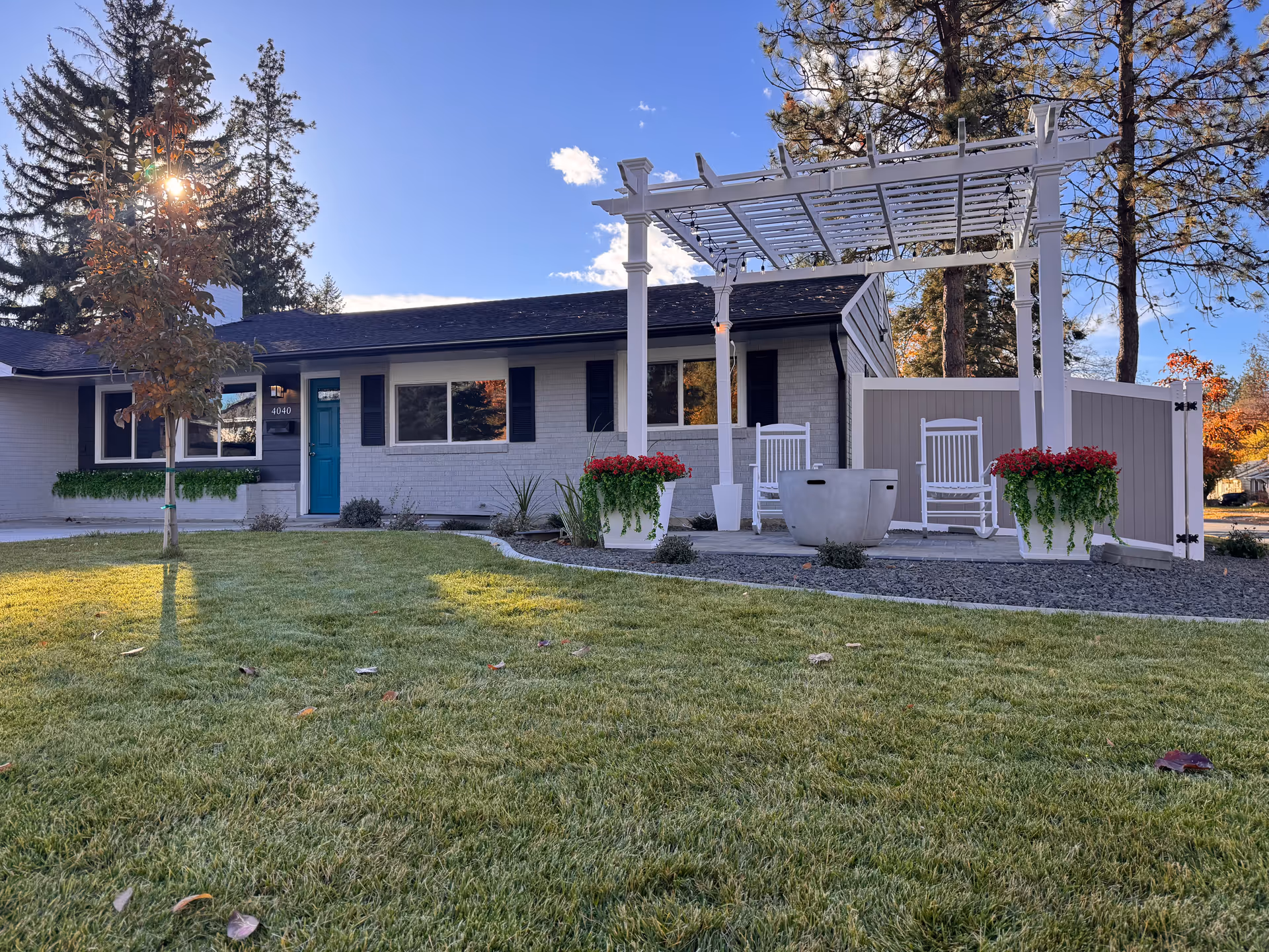 Single-story adult family home exterior with a white pergola, seating, and manicured lawn.