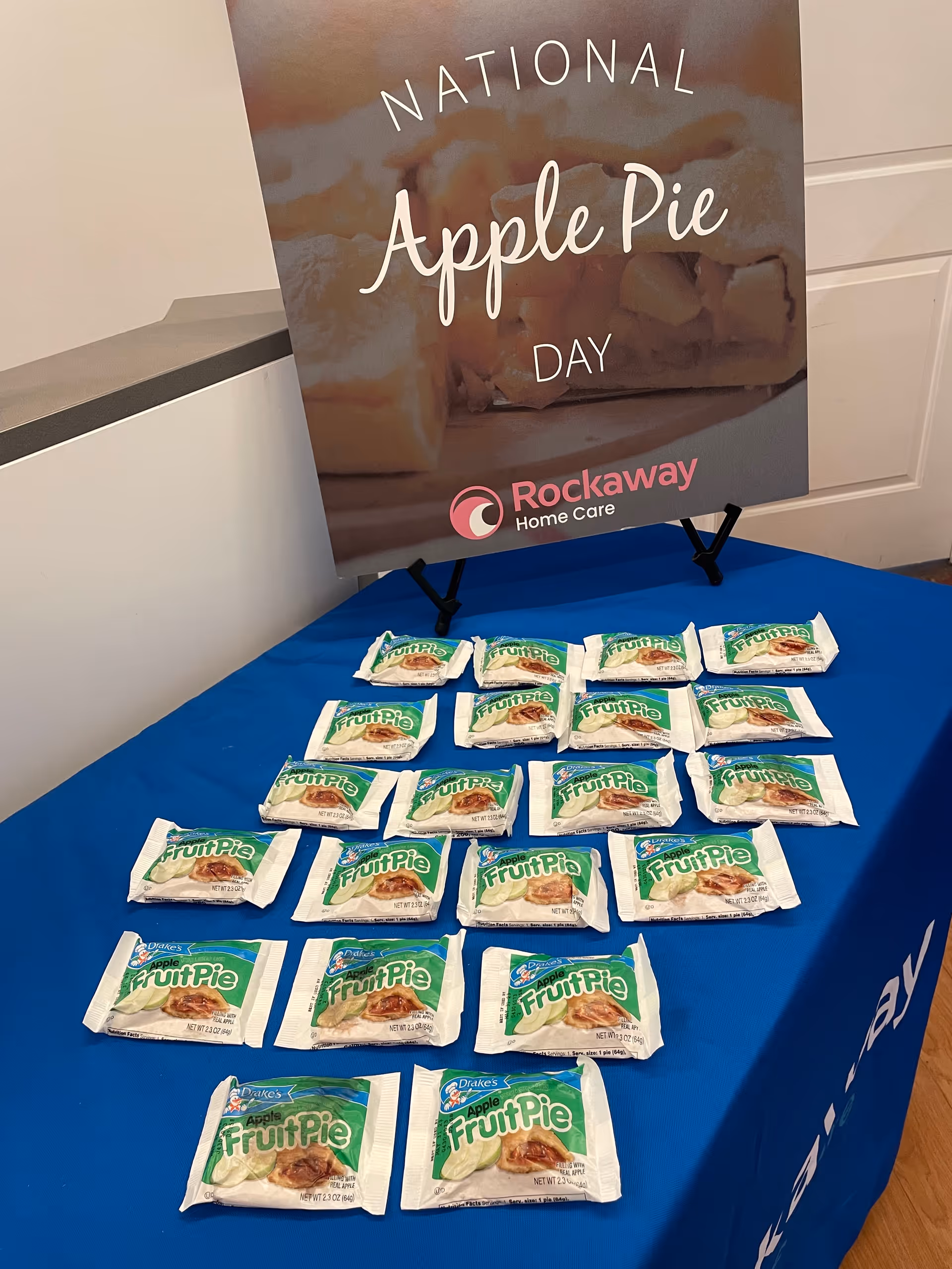 Indoor event table with Apple Pie Day poster and numerous packaged fruit pies.