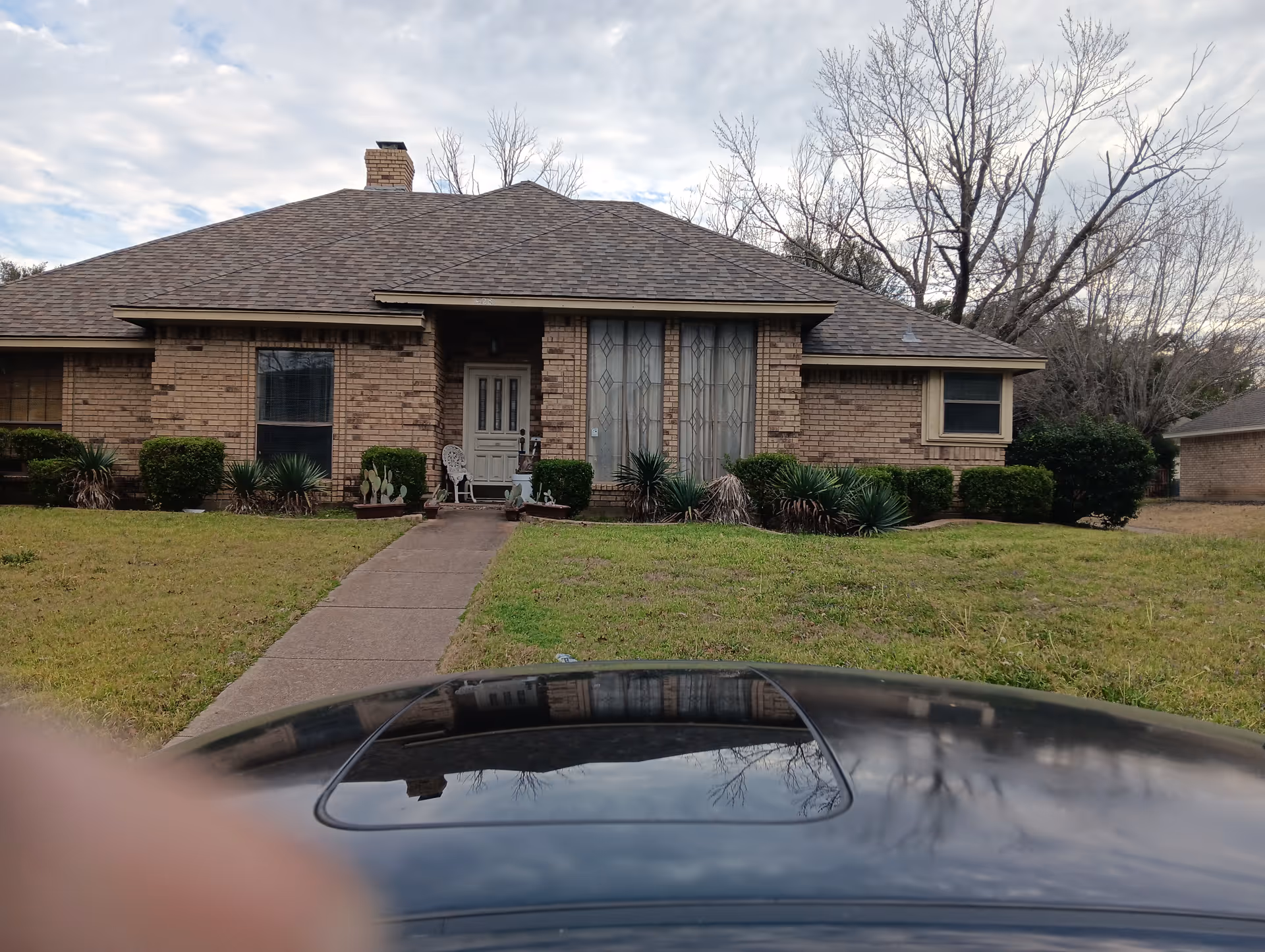 Front view of a single-story brick home with a walkway and car hood visible