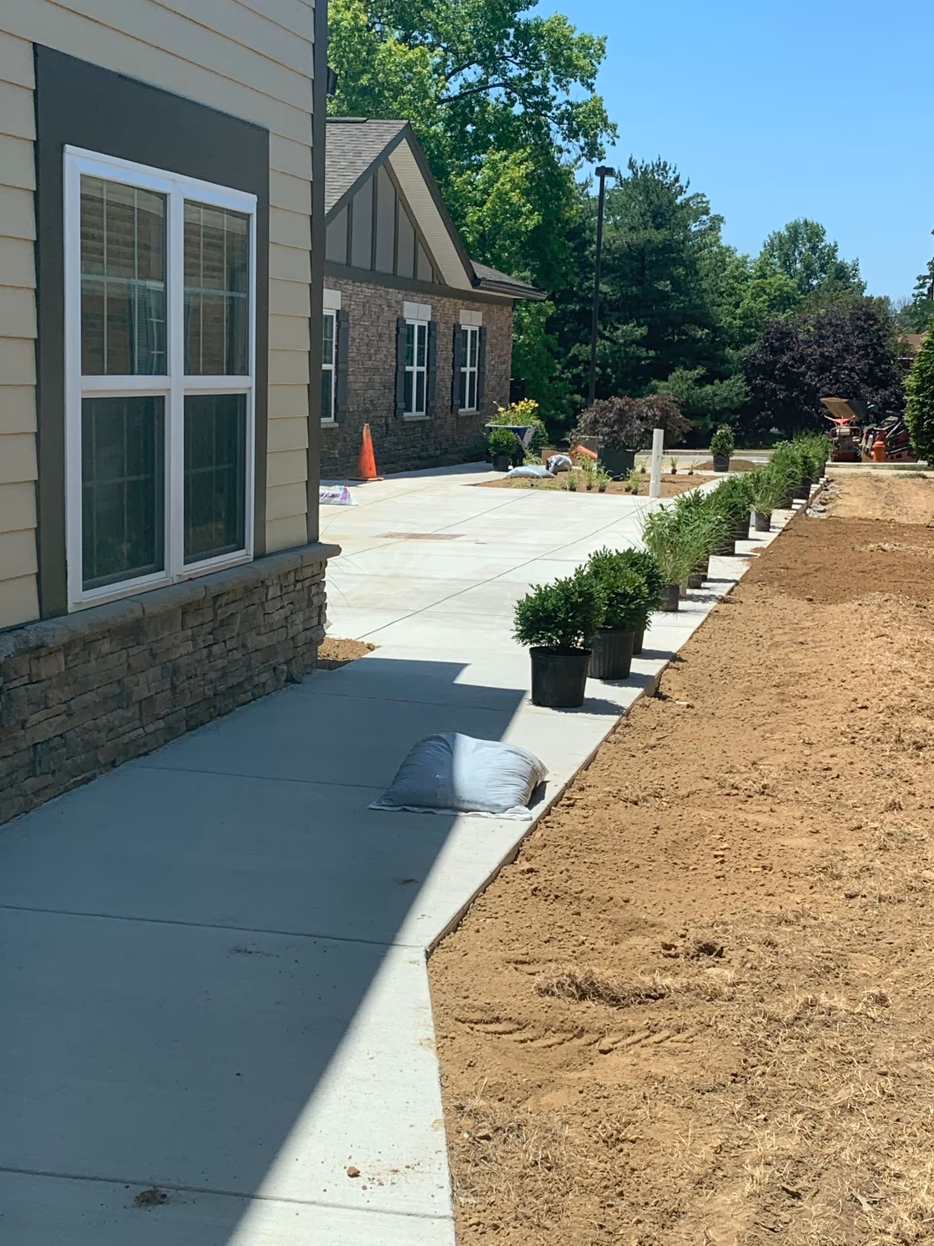 Exterior walkway beside a building with potted plants and dirt landscaping.