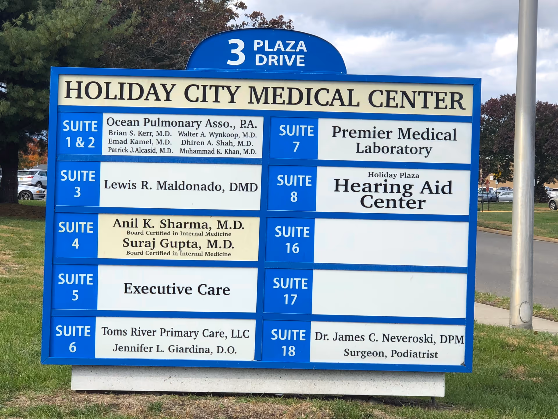 Large blue and white outdoor sign listing suites at Holiday City Medical Center.