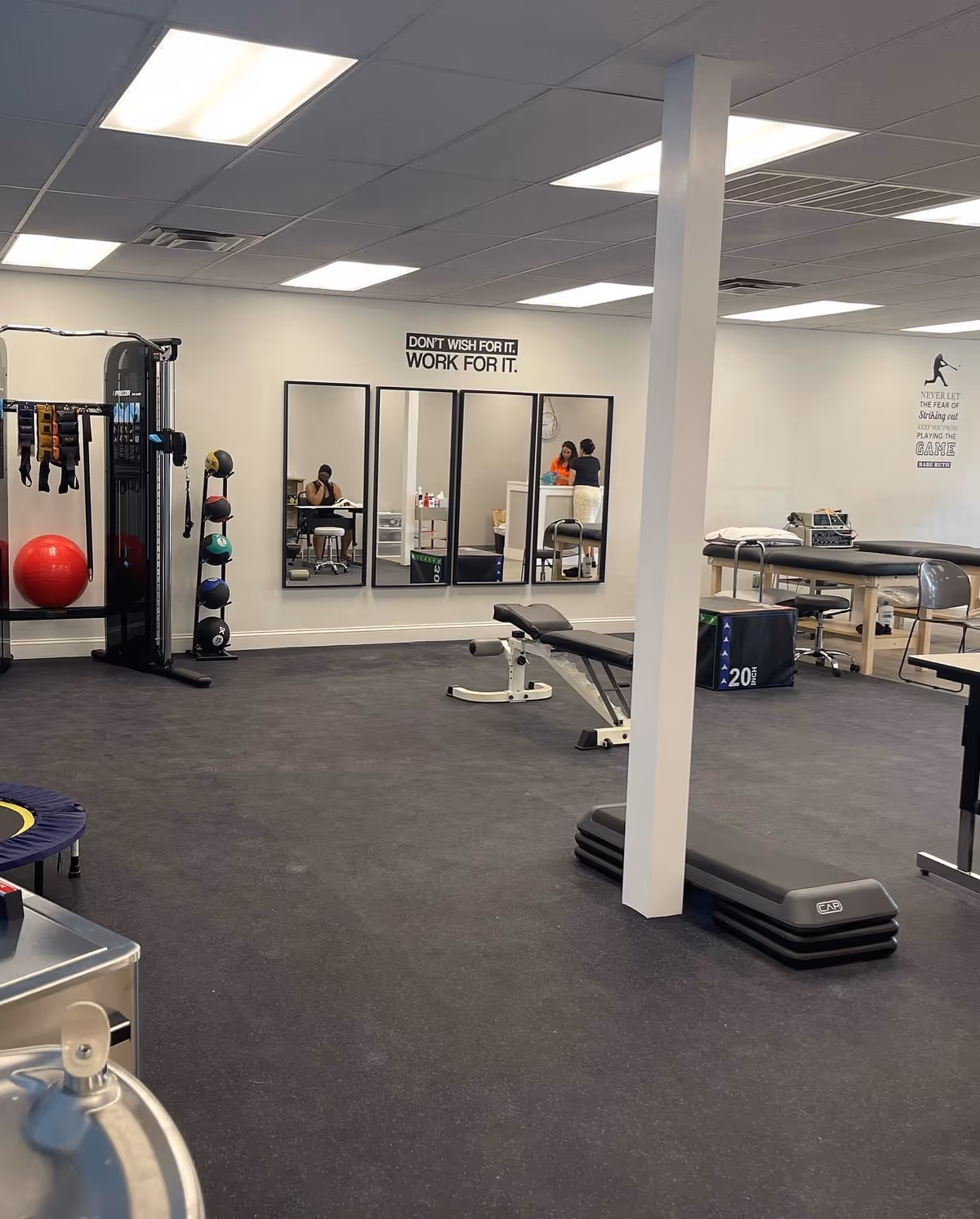 A gym/therapy space with mirrors, exercise equipment, and people visible in reflections.
