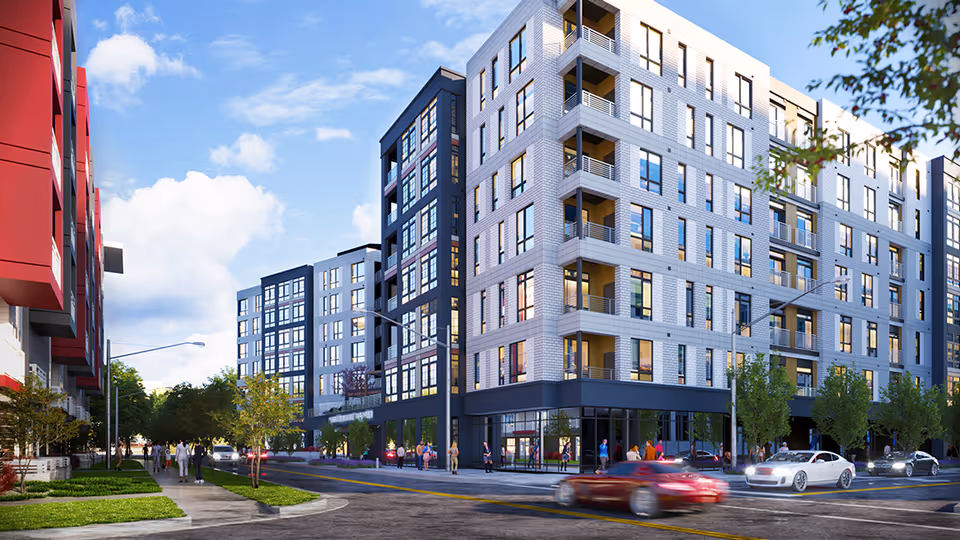 Modern multi-story residential building with large windows and balconies on a sunny day, with cars driving on the street and people walking on the sidewalks.