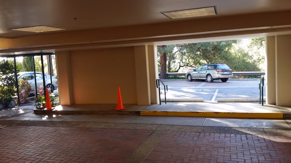 Covered building entrance/drive-through area with traffic cones, planters, and a car parked outside.