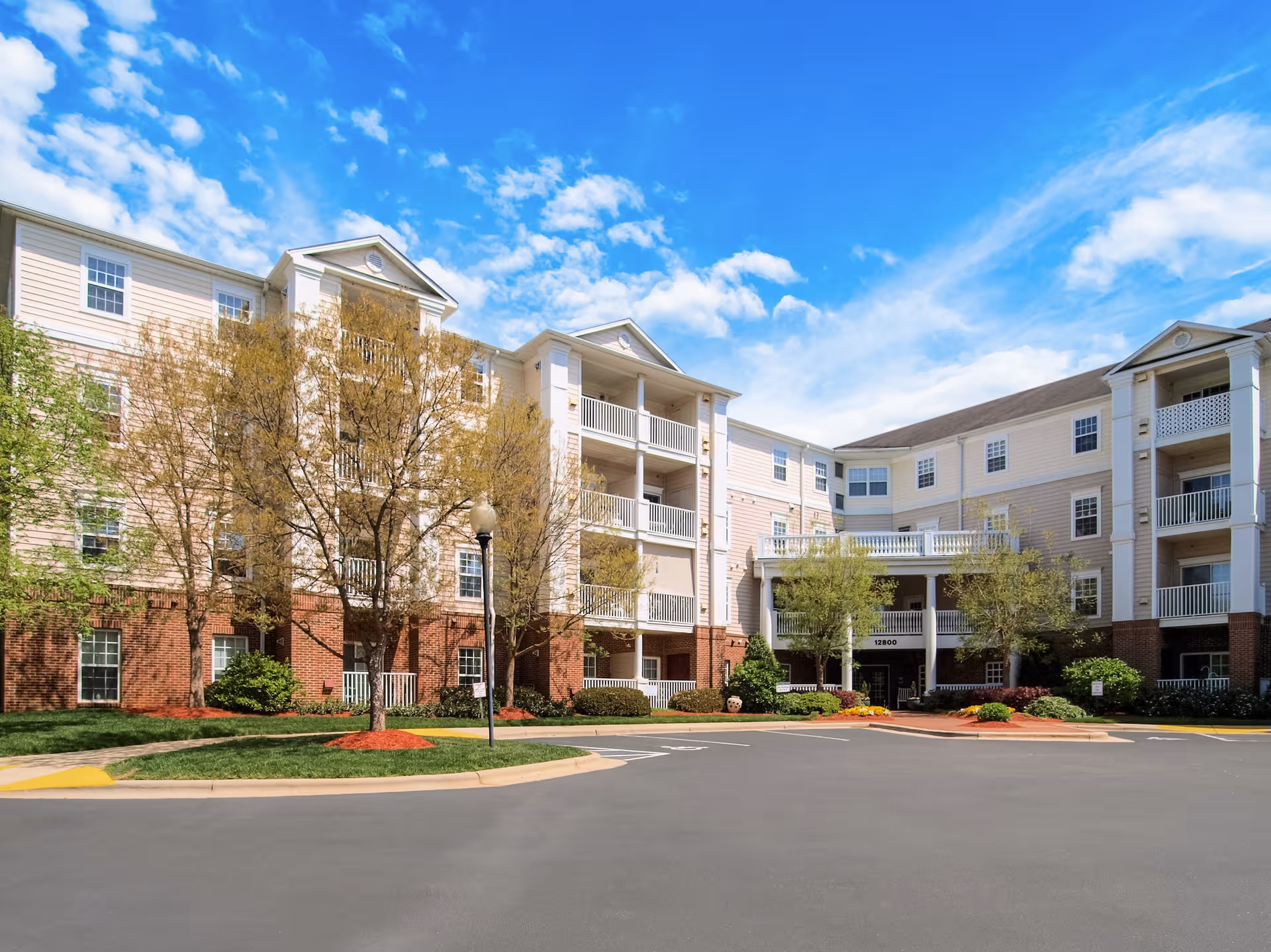 Exterior view of Gardens at Wakefield building with beige siding, brick base, and landscaped entrance.
