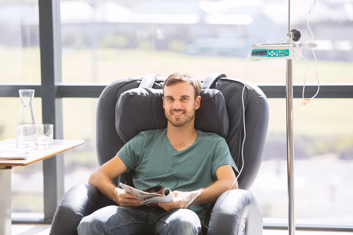 Man sits in a recliner with an IV drip in a bright clinic room.