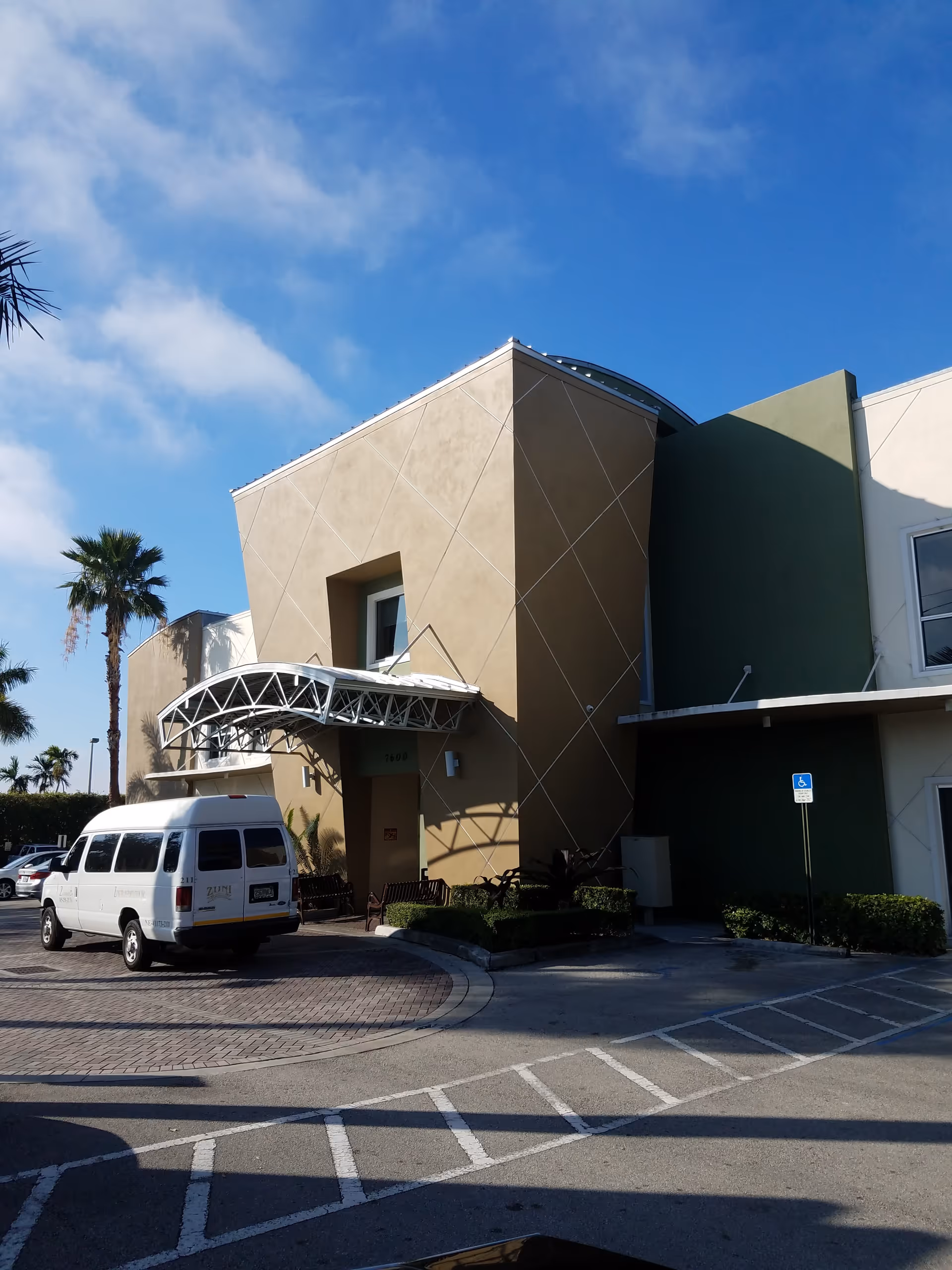 Exterior view of a modern medical facility with a beige facade and a parked white van.