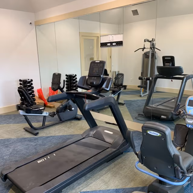 Interior fitness room with treadmills, stationary bikes, free weights, and mirrored walls.