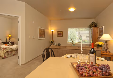 Dining area with a wine bottle and grapes on a counter; living room and bedroom visible.