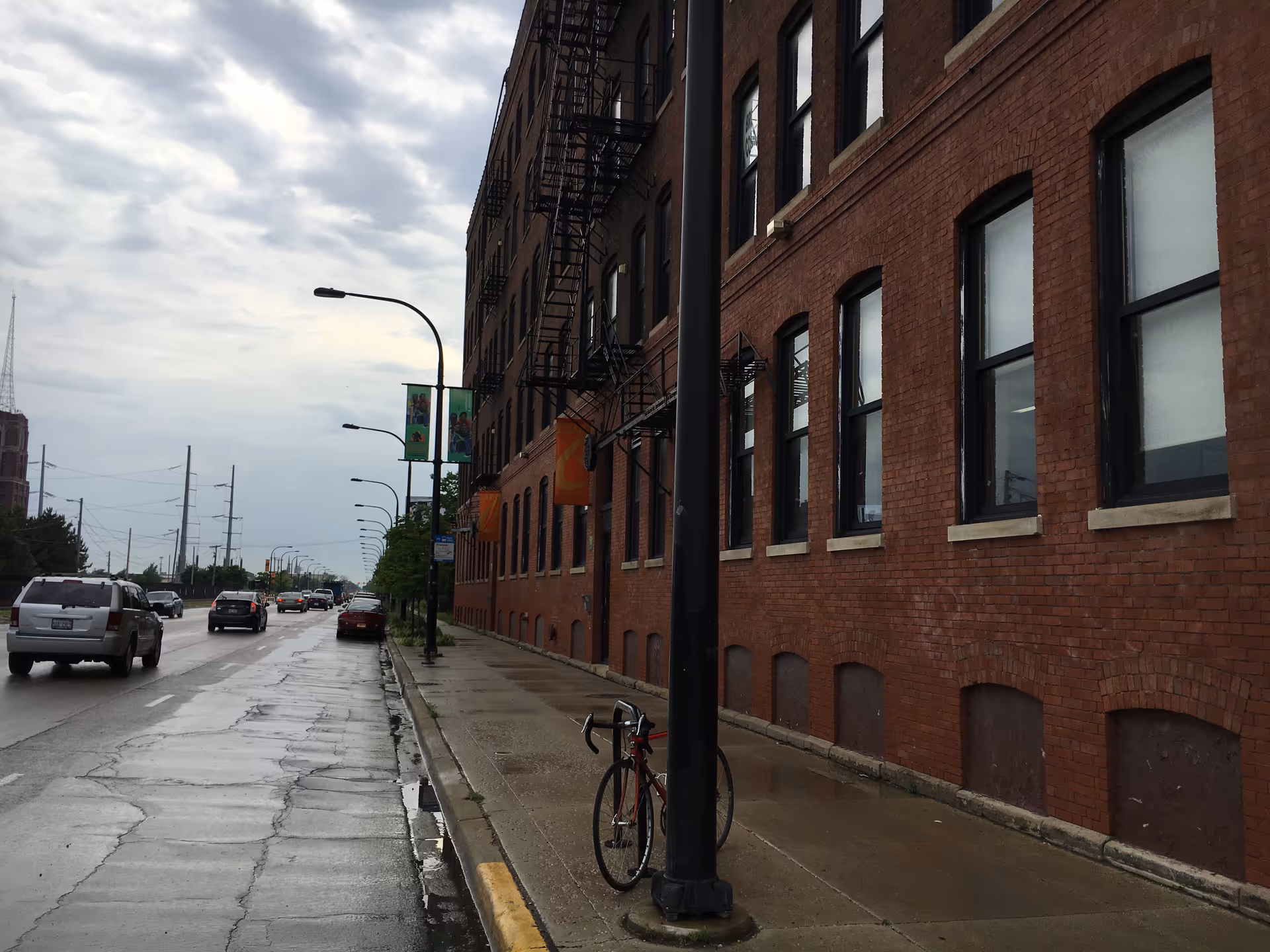 Urban street view with a brick building, sidewalk, parked cars, and a bicycle.