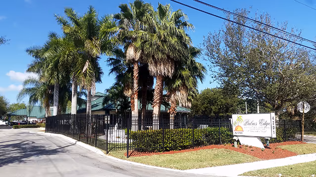 Exterior view of Hidden Pines Assisted Living entrance with palm trees and a gated walkway.