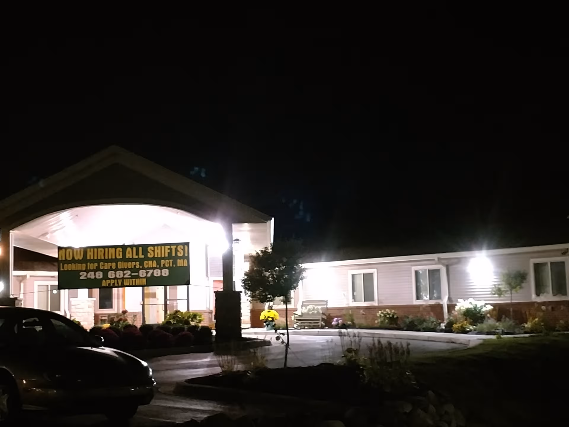 Night exterior view of Waterford Oaks Senior Care West entrance with an illuminated hiring banner visible.