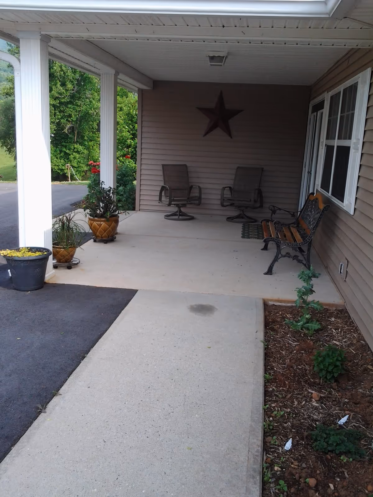 Covered front porch with two swivel chairs, a bench, potted plants, and a decorative star on the wall.
