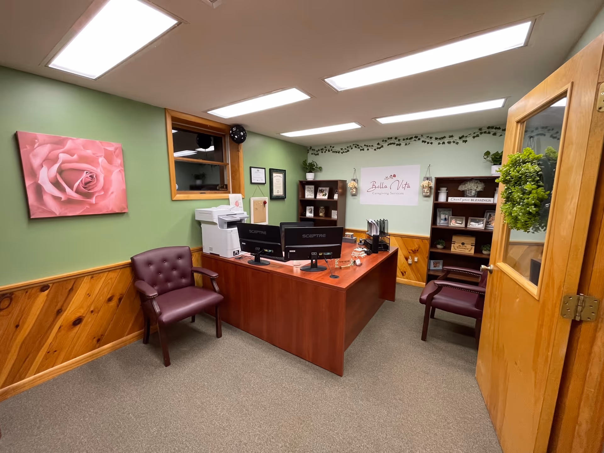 Reception desk with computers, printer, and burgundy chairs in a green-walled office.