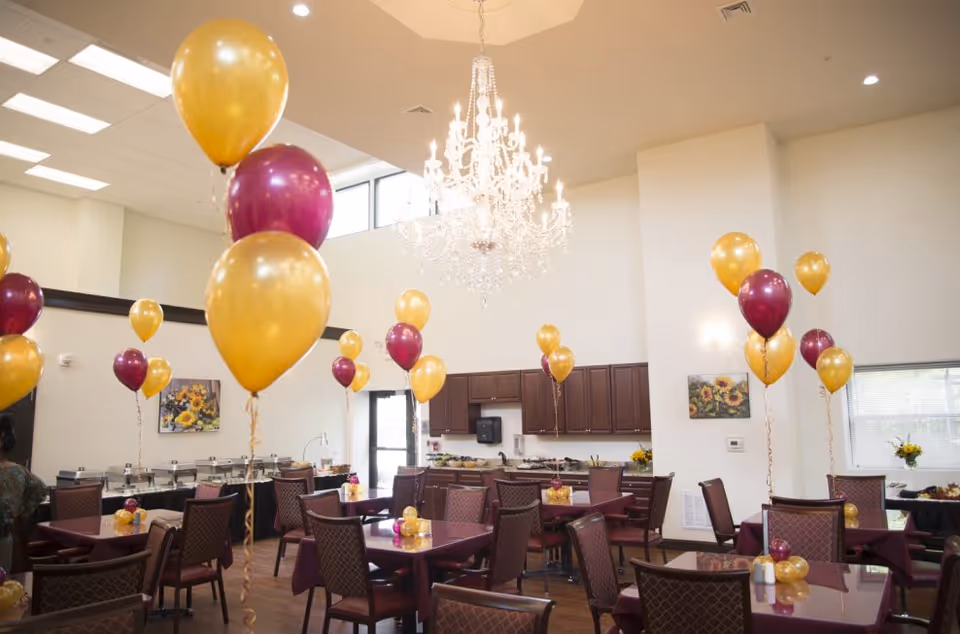 Interior dining room decorated with maroon tablecloths, balloons, and a chandelier.