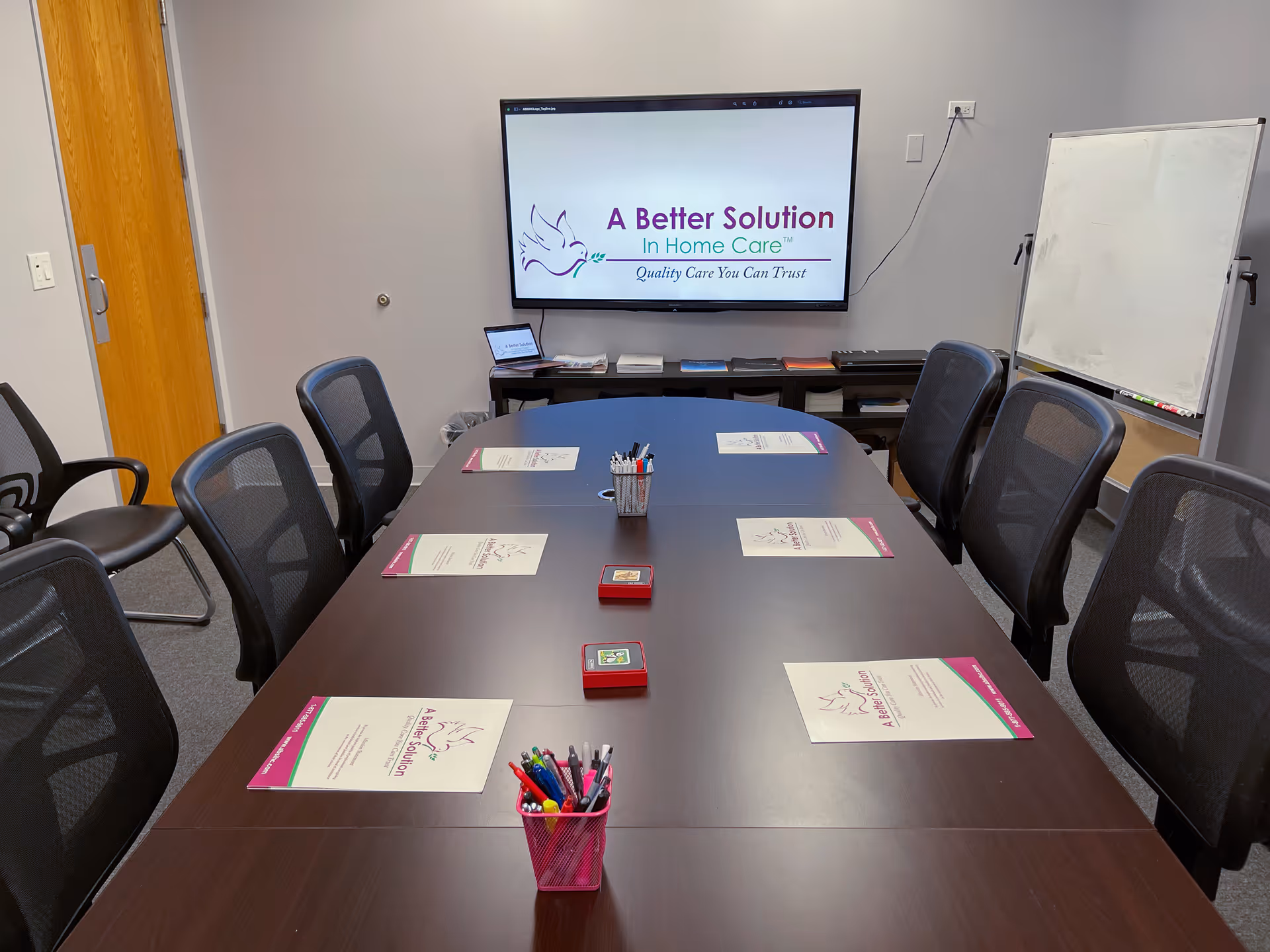 Conference room with long table, chairs, and a screen displaying A Better Solution In Home Care.