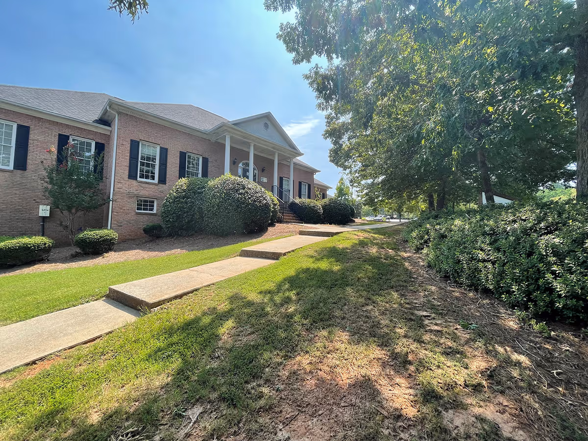 Brick senior living facility exterior with steps, hedges, and a sunny walkway.