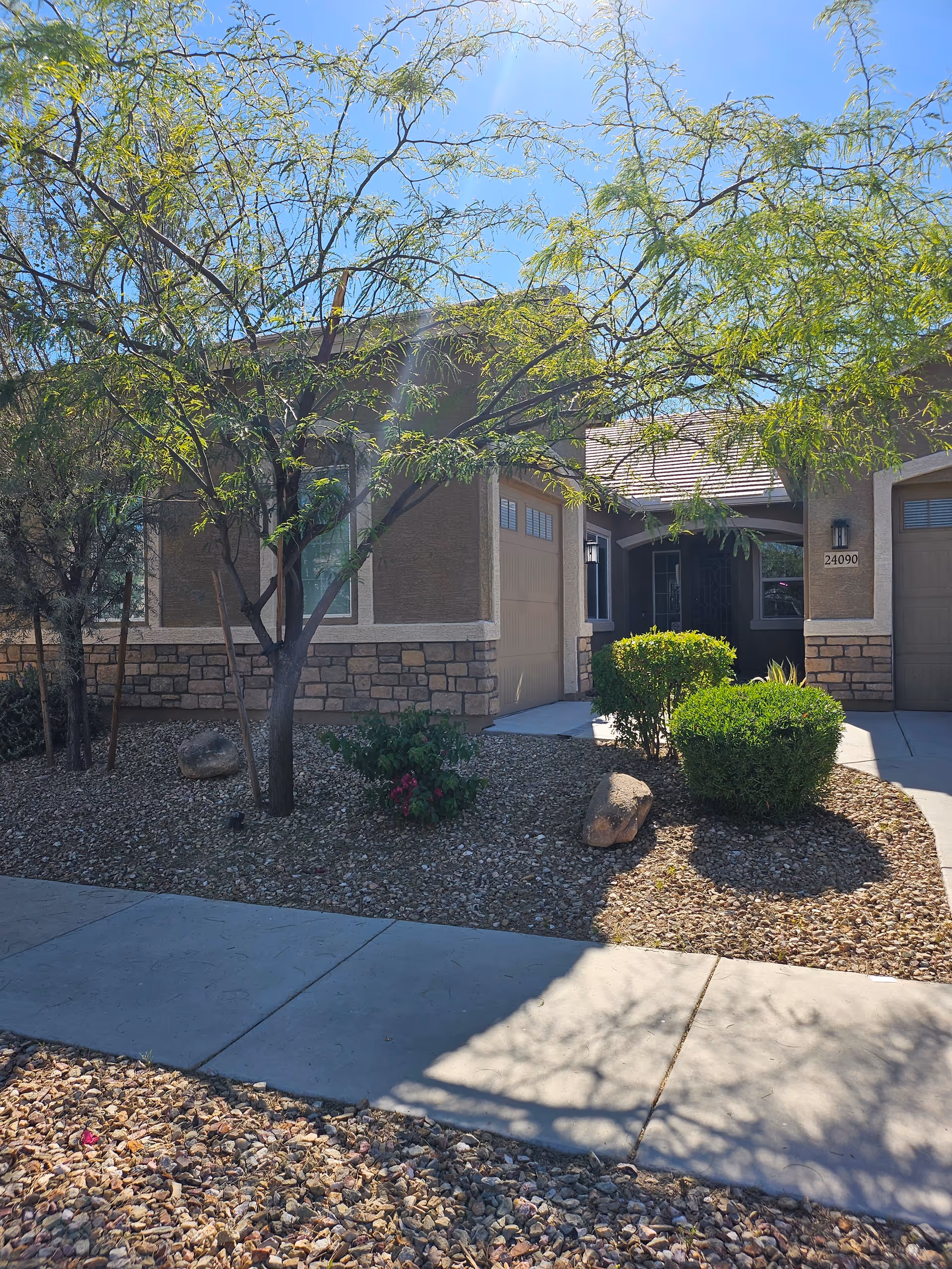 Front exterior of a beige assisted living residential building with desert landscaping and a sidewalk.