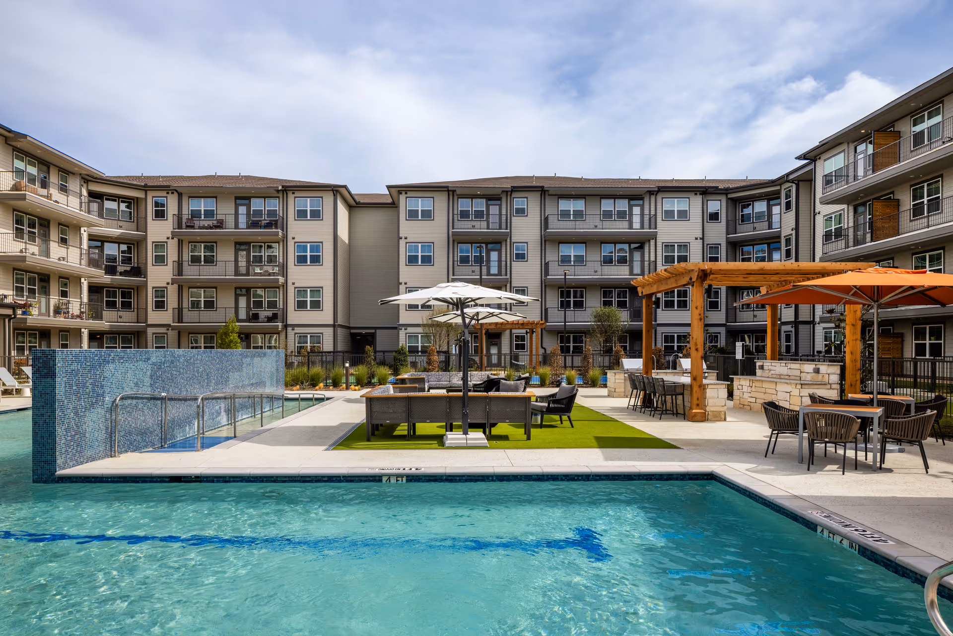 Outdoor pool area surrounded by residential buildings with umbrellas and seating.
